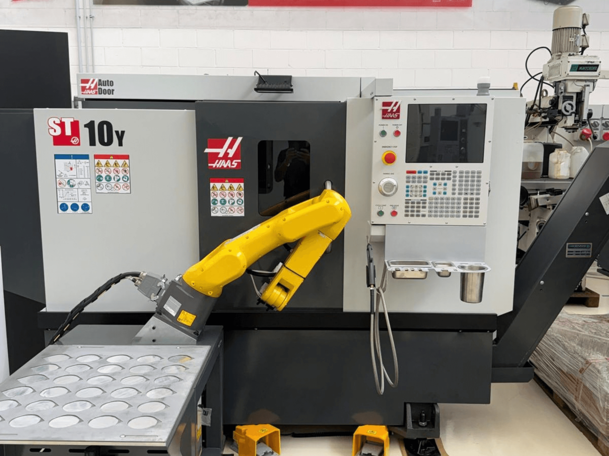 Tornio orizzontale Haas ST-10Y visto frontalmente, dotato di braccio robotico e pannello di controllo con vassoi portautensili.