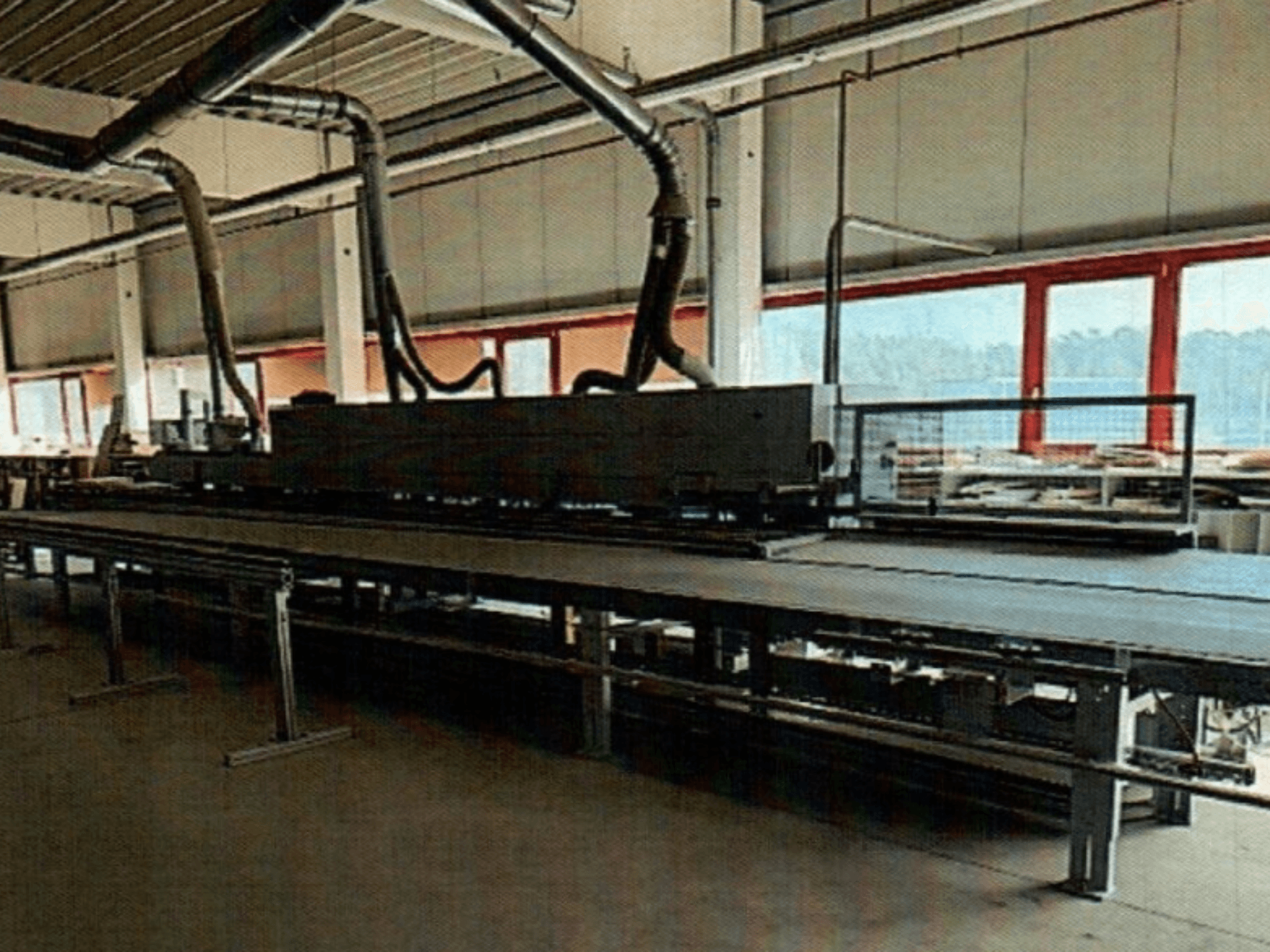 La bordatrice HOMAG KAL 370 in un'officina, vista laterale, che mostra il lungo piano di lavoro piatto con i condotti di ventilazione sovrastanti.