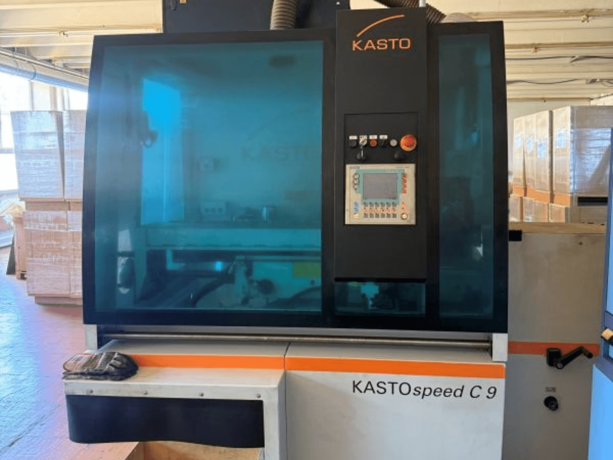 Vista frontale della sega circolare per metalli KASTO KASTOspeed C 9, con pannello di comando e vetro di protezione, con casse di legno sullo sfondo.