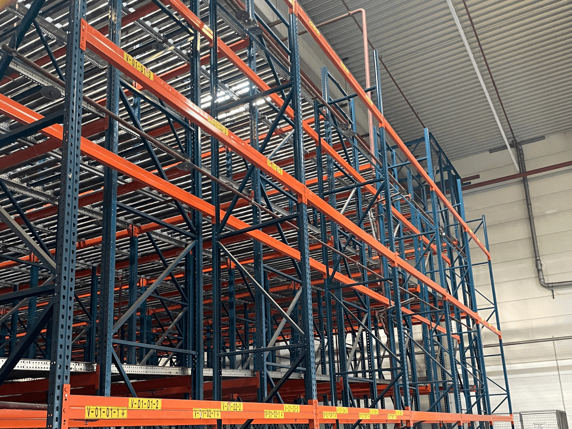 FL SYSTEME F05.10 Sistema di movimentazione pallet FLG in un magazzino, visto lateralmente, con scaffalature arancioni e blu per carichi pesanti.