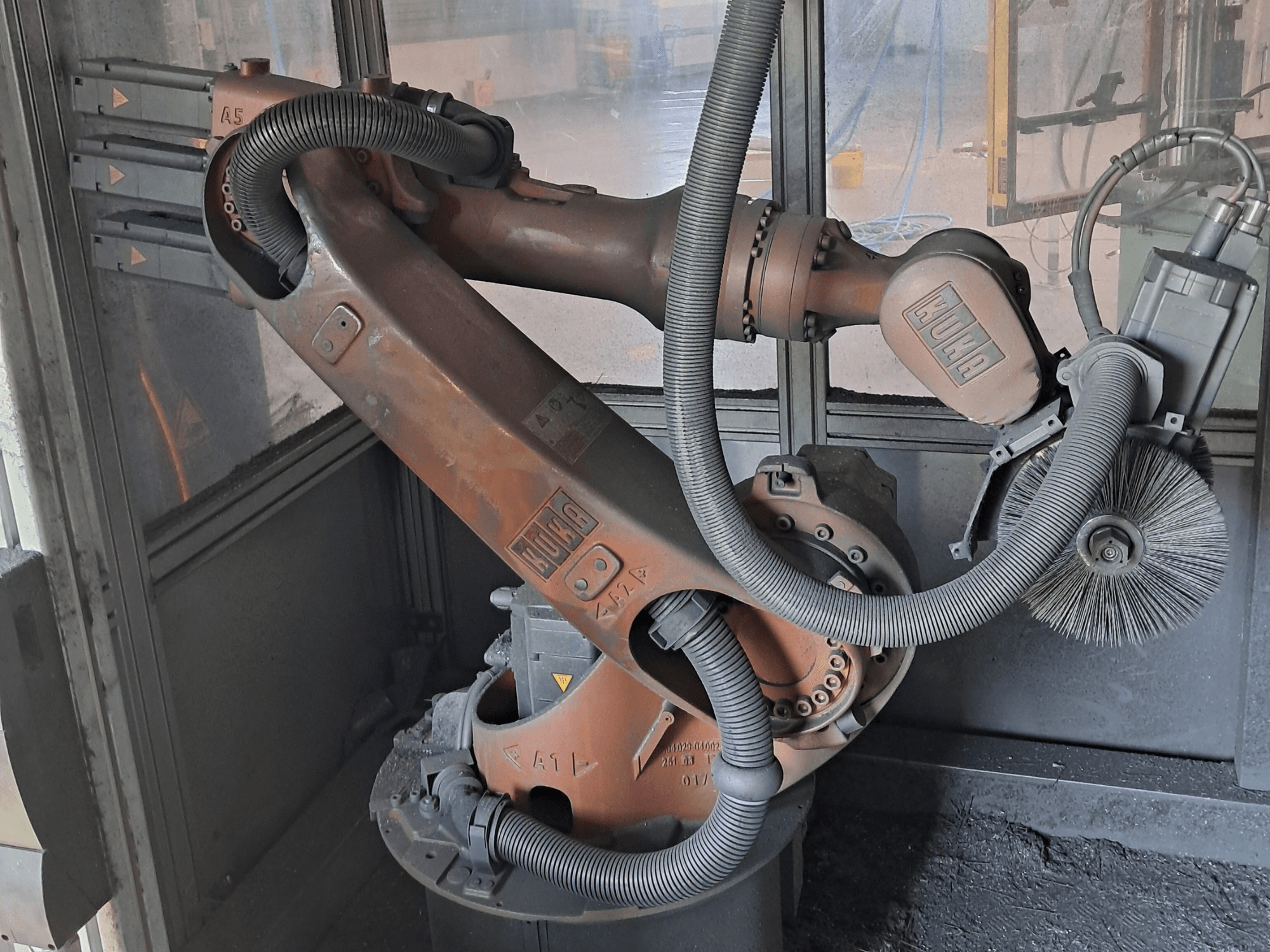 Braccio robotico KUKA KR 16-2 visto di profilo, con cavi, spazzole e giunti meccanici in evidenza, inserito in un ambiente di lavoro.