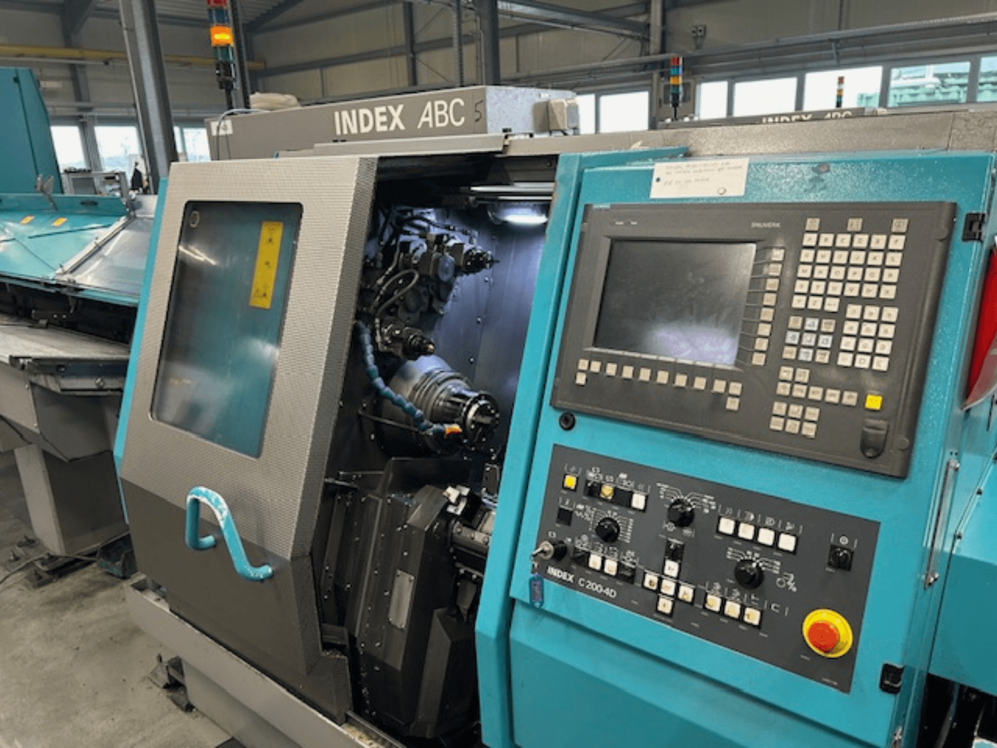 Vista frontale di un tornio CNC INDEX C200-AD con pannello di controllo, componenti interni visibili e caratteristiche di sicurezza.