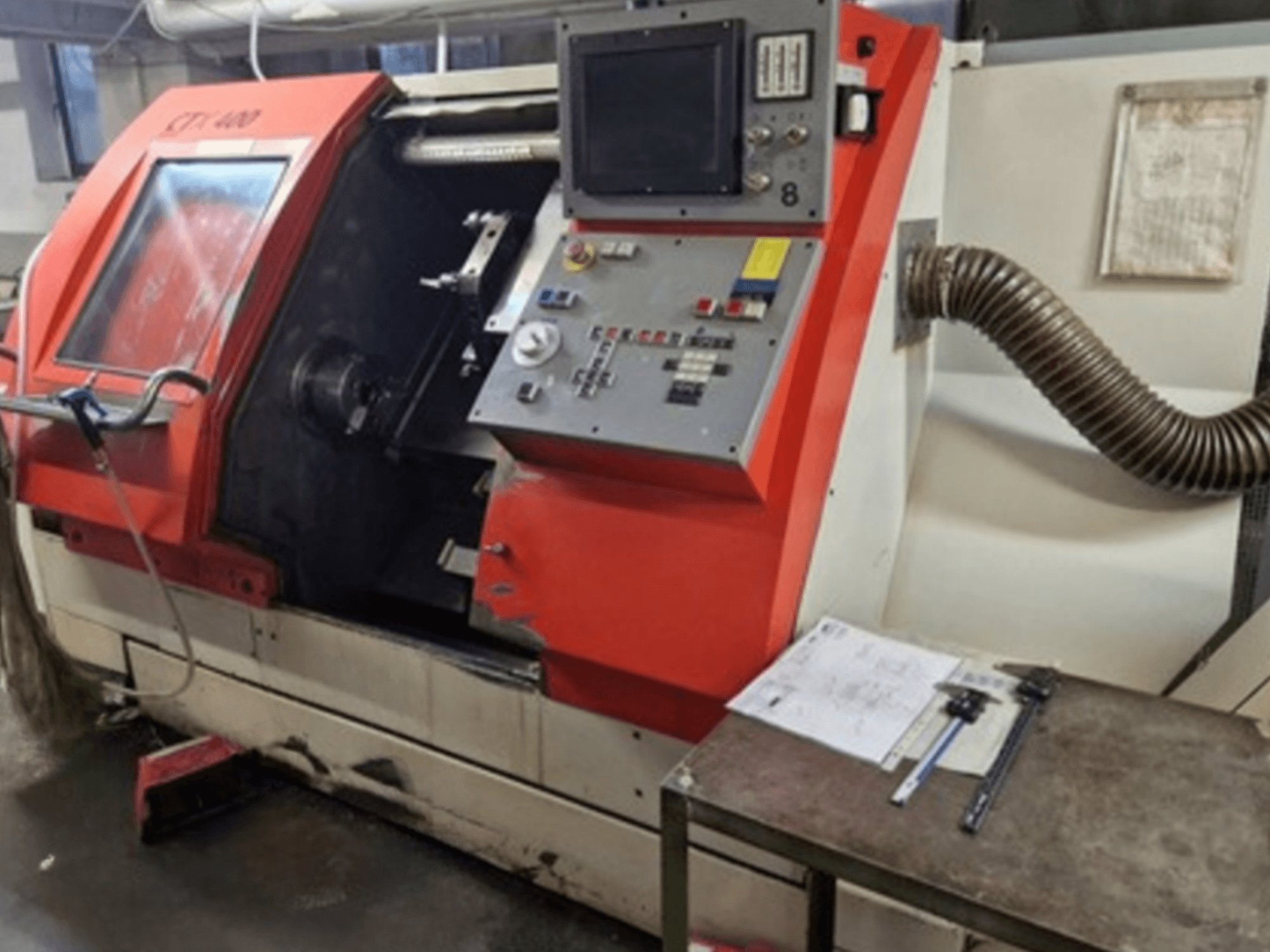 Tornio orizzontale Gildemeister CTX 400, vista frontale con pannello di controllo e tubo di scarico. Include strumenti di misura sul tavolo.