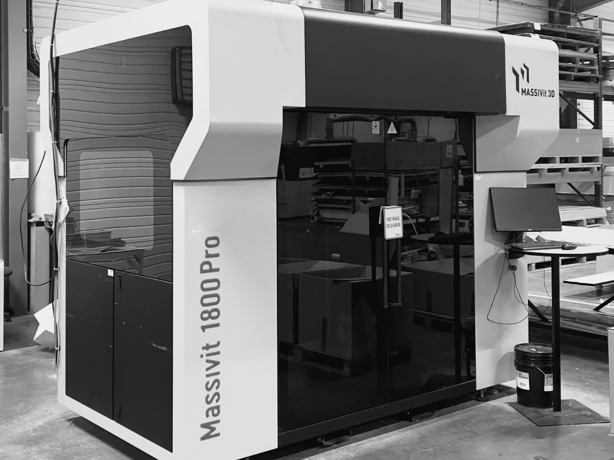 Stampante 3D in plastica MASSIVIT 1800 PRO in un laboratorio, vista frontale, con postazione computer e pannello di controllo visibili.