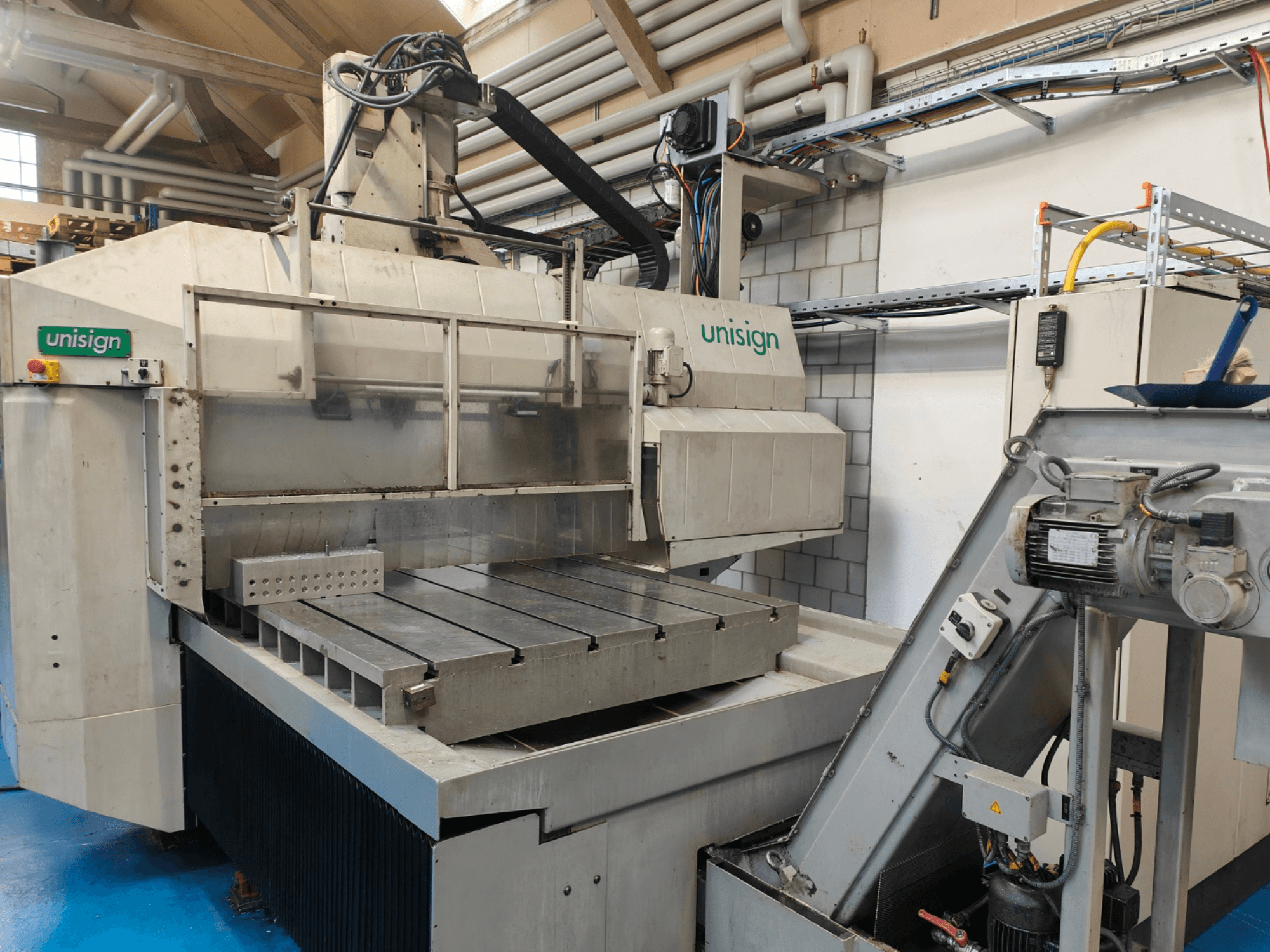 Macchina CNC Unisign in un'officina, vista frontale, con grande tavolo, pannello di controllo ed elementi di design industriale.