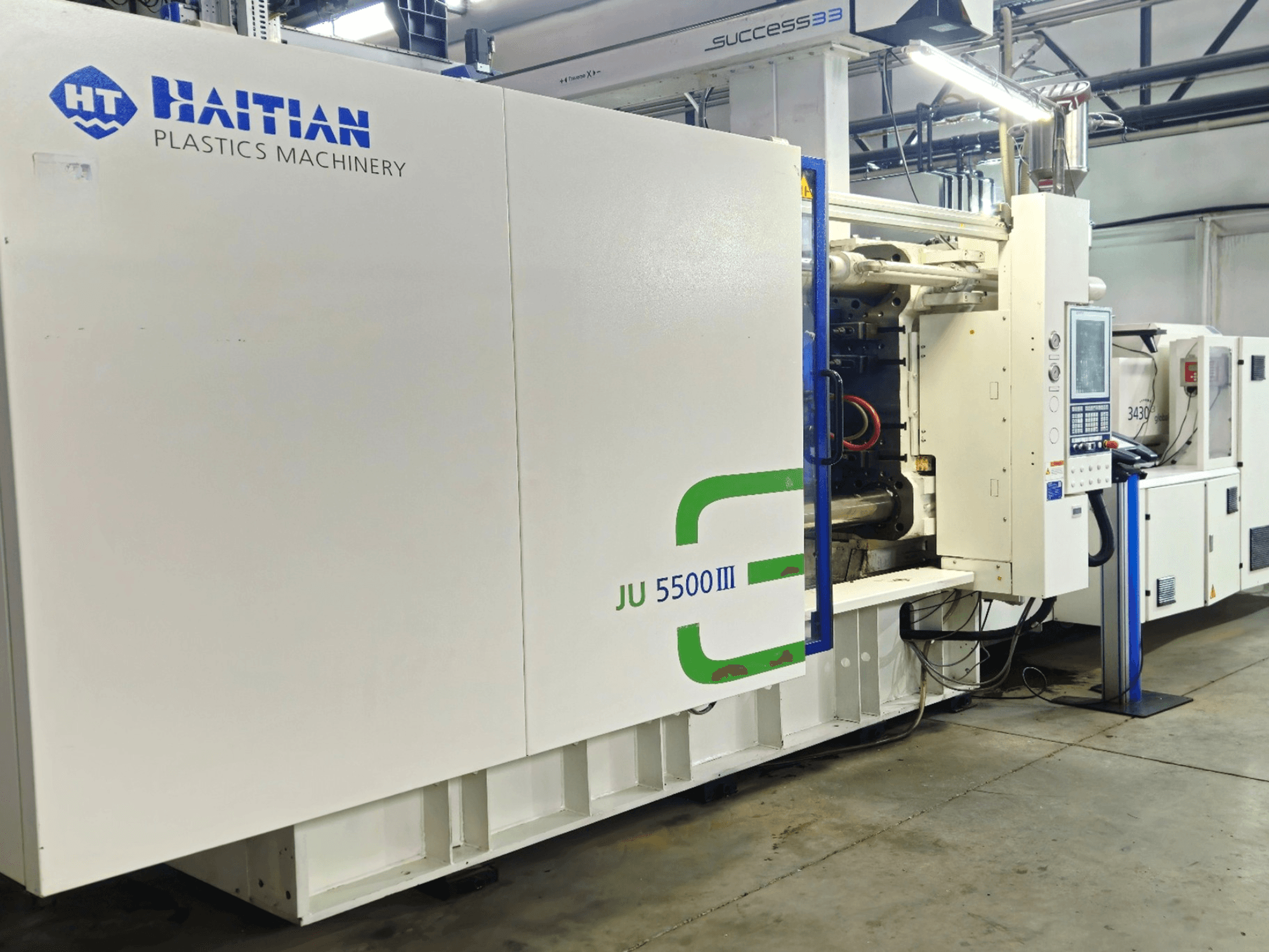 Macchina per materie plastiche JU 5500III di Haiti in un ambiente di fabbrica, vista frontale che mostra il pannello di controllo e l'area di produzione.