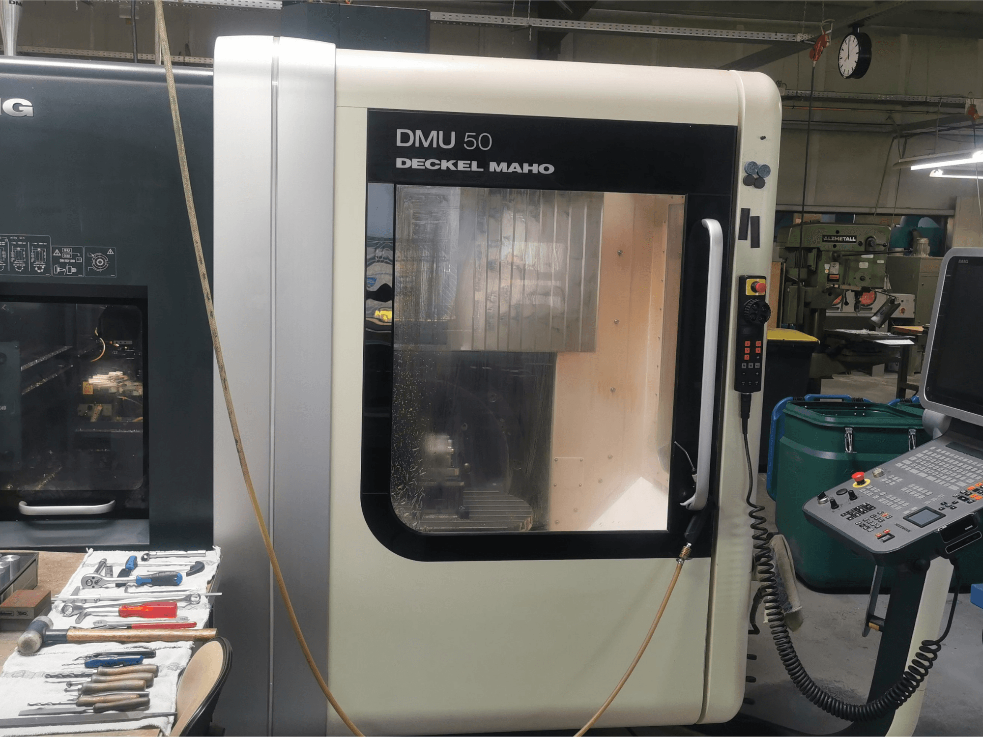 Macchina CNC DMU 50 deckel maho vista frontalmente, con il pannello di controllo e la porta trasparente. Gli utensili sono vicini.