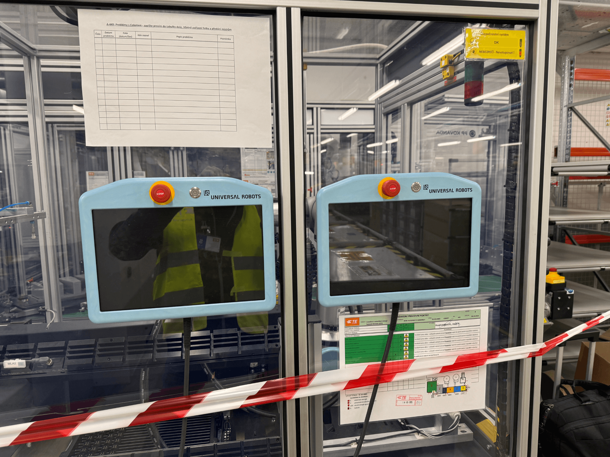 Pannello di controllo per il braccio robotico Universal Robots UR5 e, con due monitor, pulsanti di arresto di emergenza e istruzioni di sicurezza.