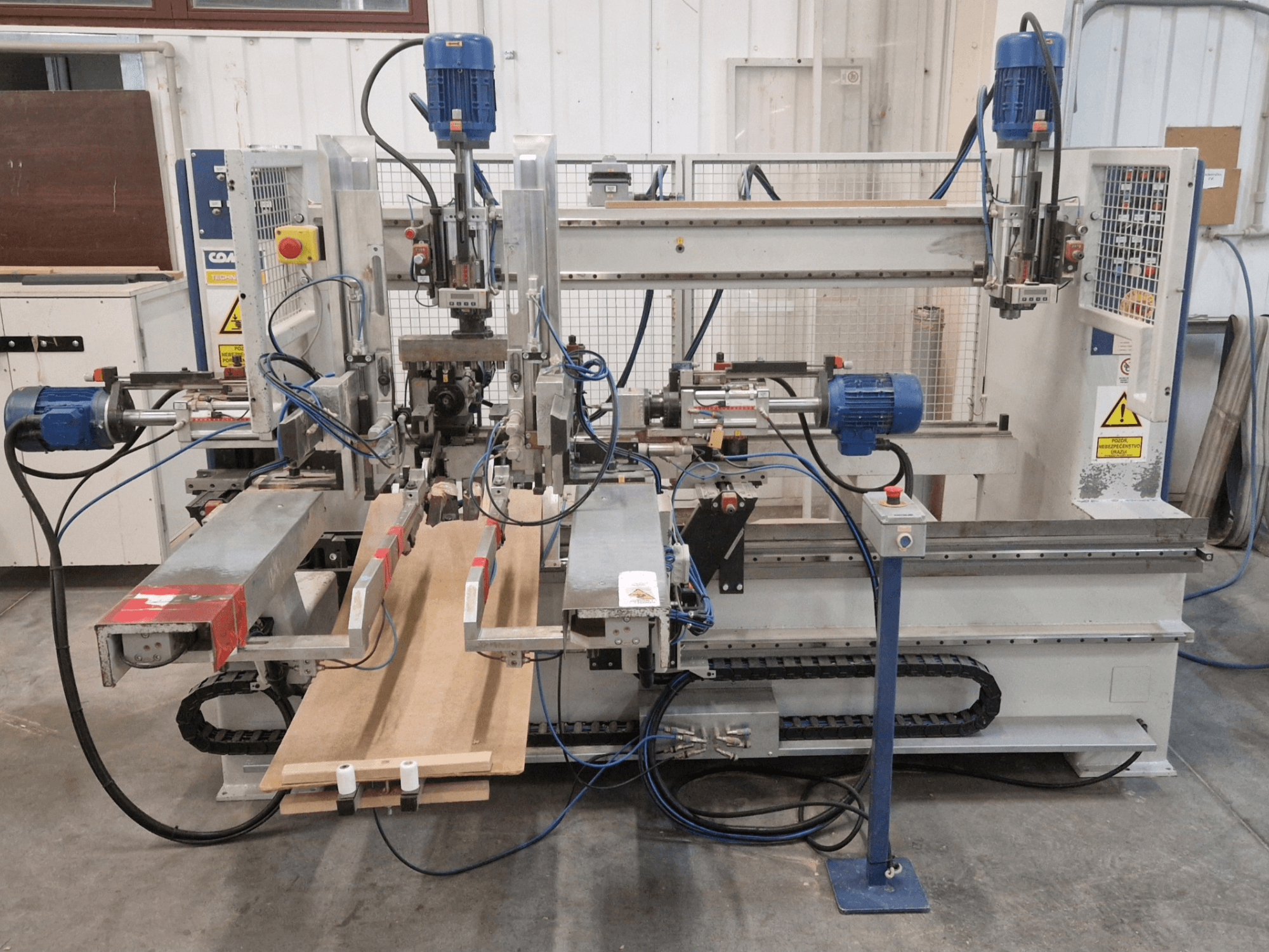 Vista frontale della foratrice multimandrino COMEC FMOV 1500, che mostra i due mandrini, il pannello di controllo e il pezzo di legno in funzione.
