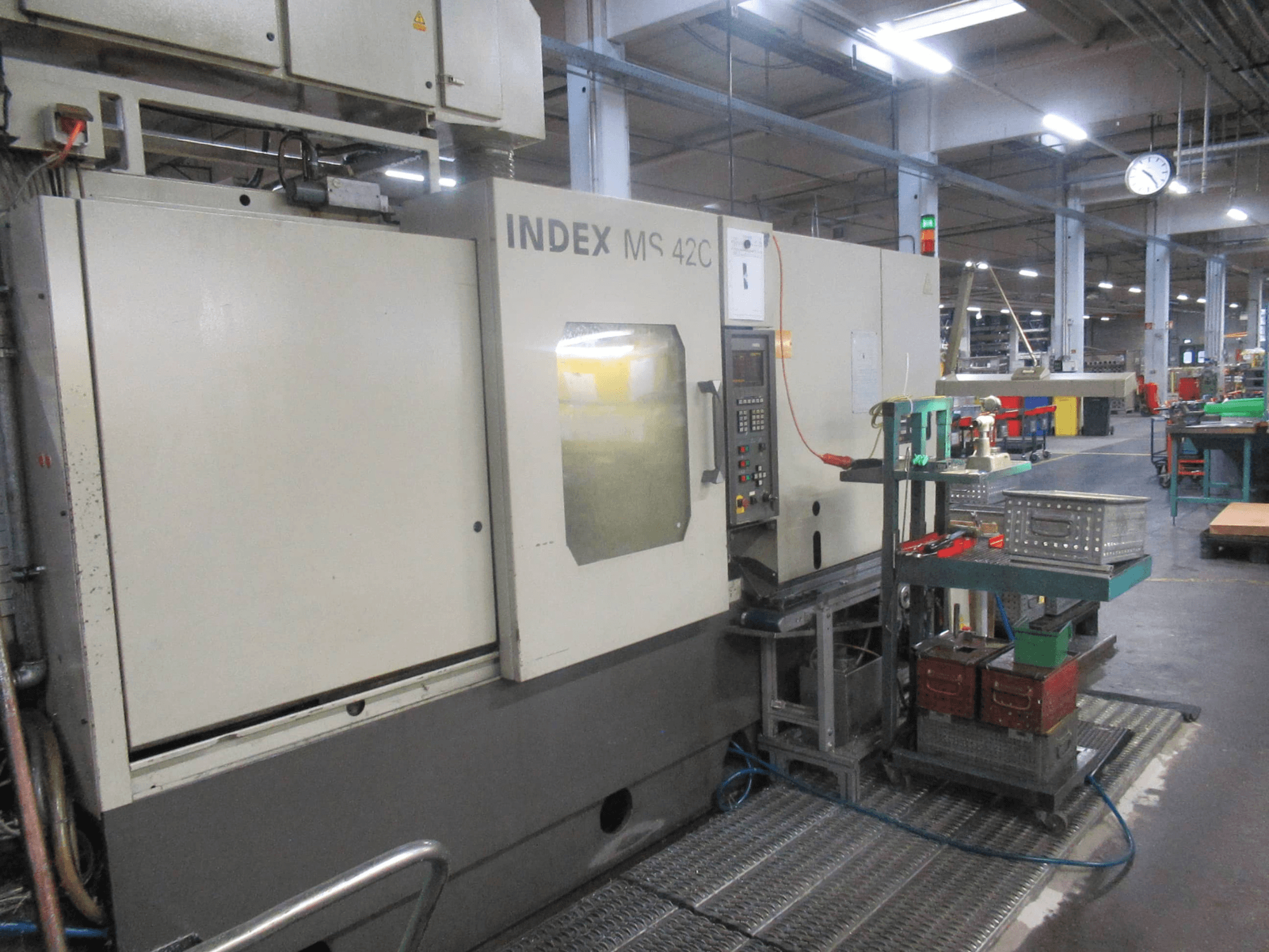 Macchina CNC INDEX MS 42C in un'officina, vista laterale che mostra il pannello di controllo e il magazzino utensili su carrello a ruote.