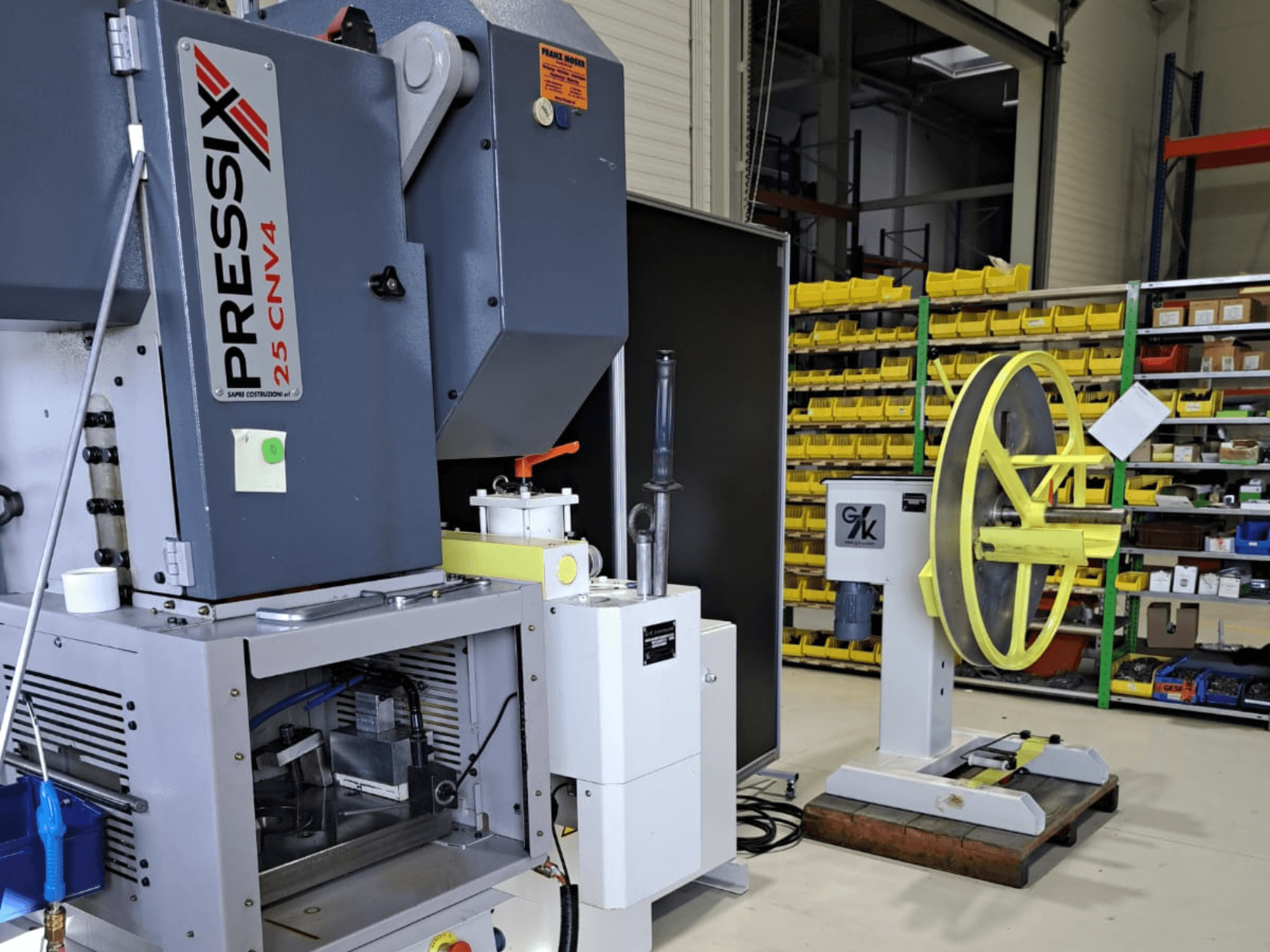 Configurazione di una macchina industriale con PRESSIX 25 CNV4 a sinistra e una ruota gialla montata su una base grigia a destra, vista frontale.