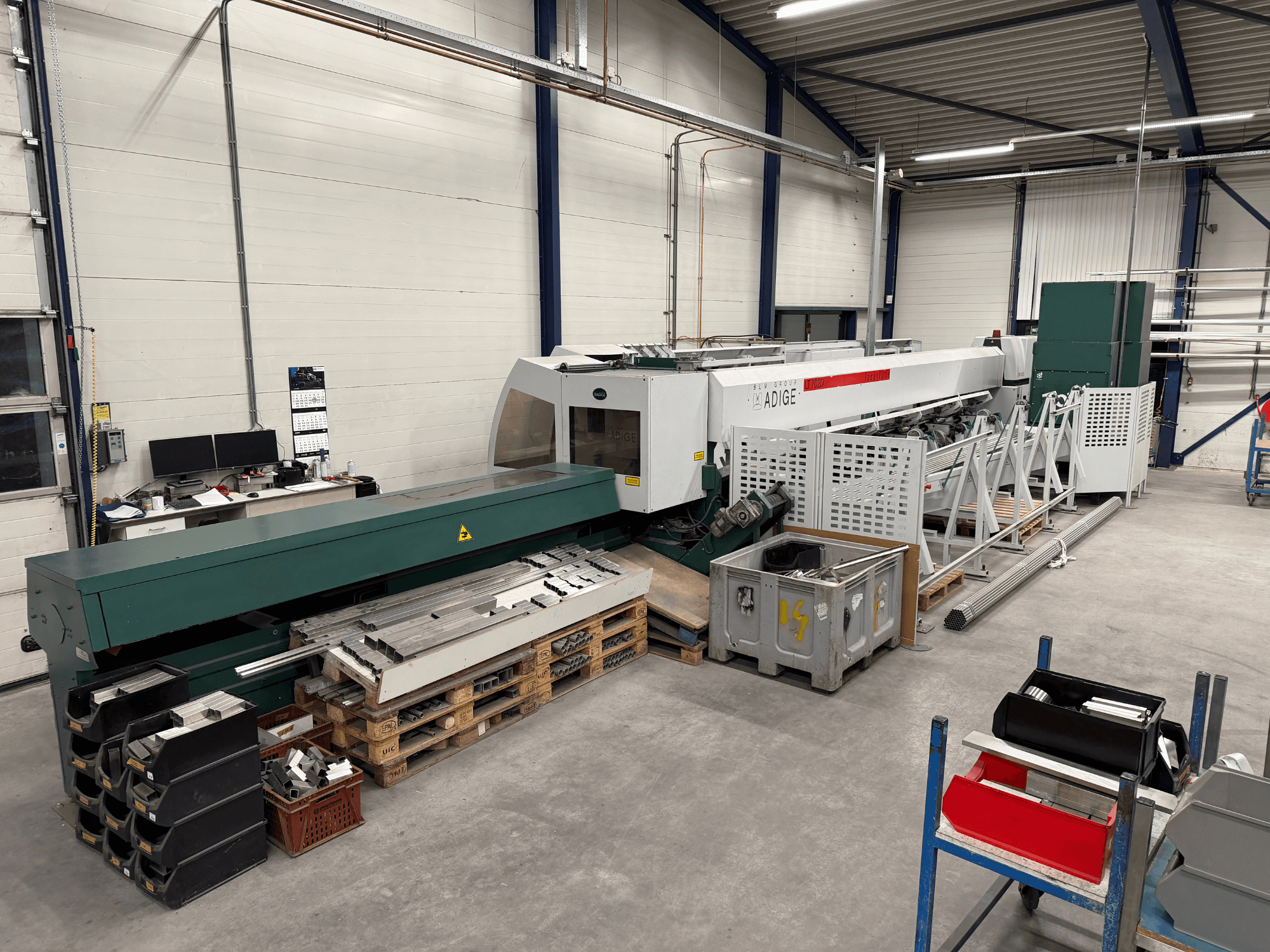 Macchina da taglio laser a CO₂ BLM Adige LT702 in un'officina, vista laterale con componenti metallici e area di lavoro ingombra.