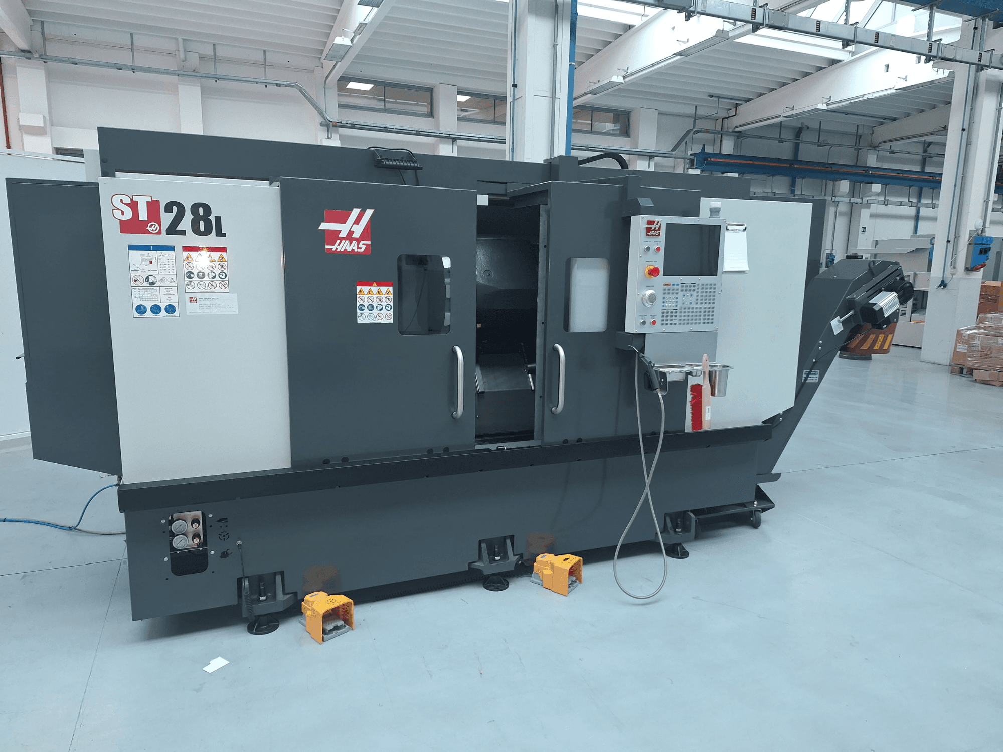 Vista laterale del tornio orizzontale Haas ST-28L, con pannello di controllo, pulsanti di comando ed etichette di sicurezza.