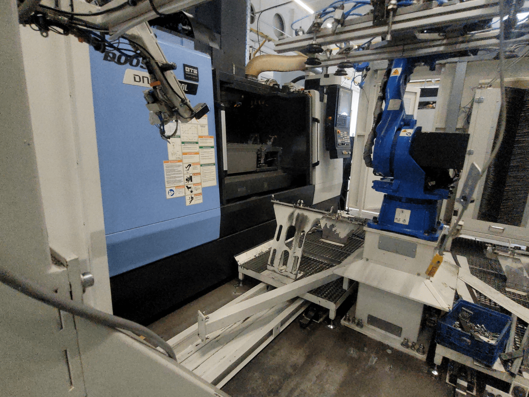 Vista laterale del centro di lavorazione verticale DOOSAN DNM 6700L, con braccio robotico e pannello di controllo visibili, che mostra la configurazione del macchinario.