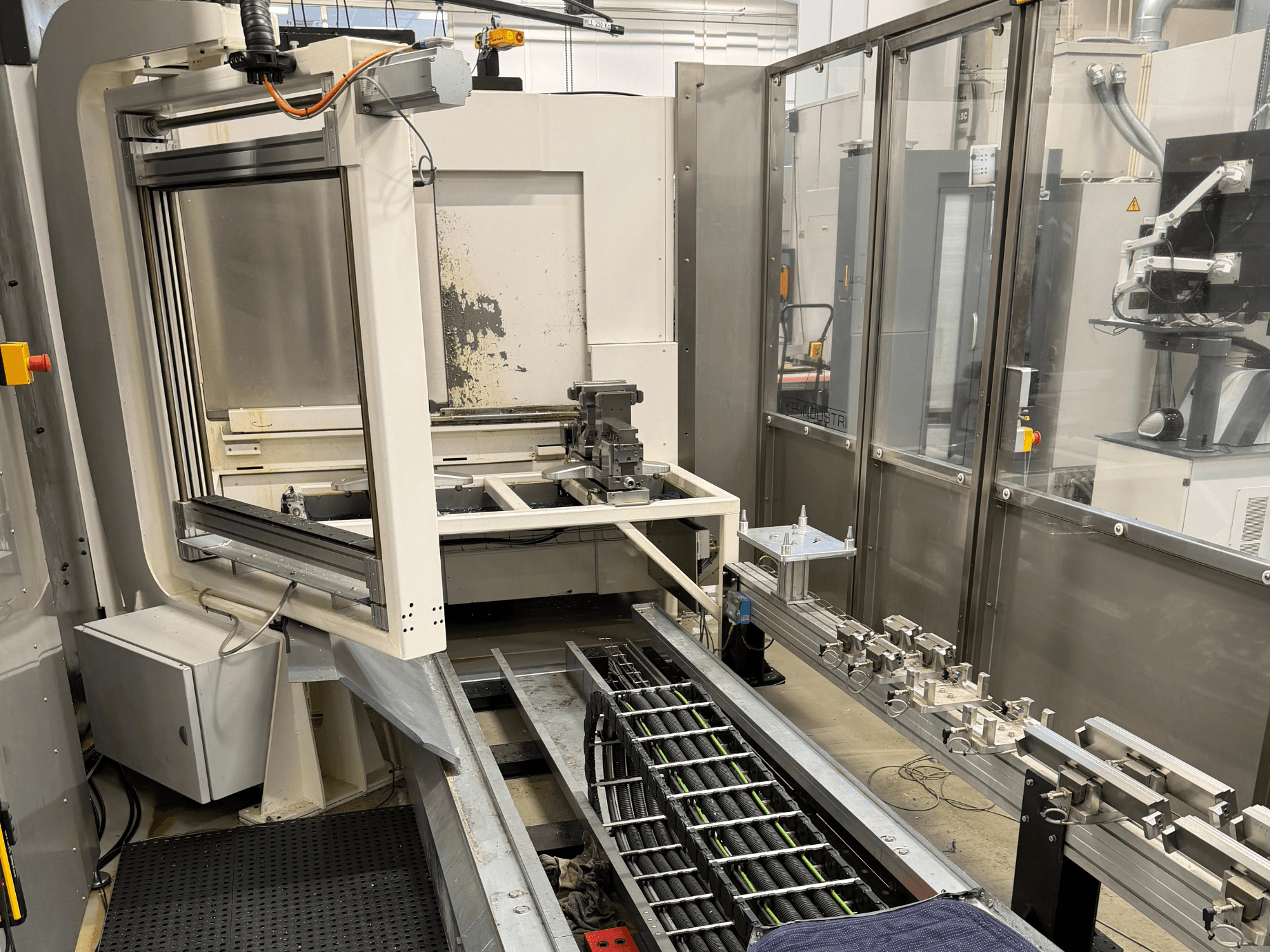 Stazione di lavoro industriale automatizzata che mostra un braccio robotico, un sistema di binari e un pannello di controllo in una vista laterale.