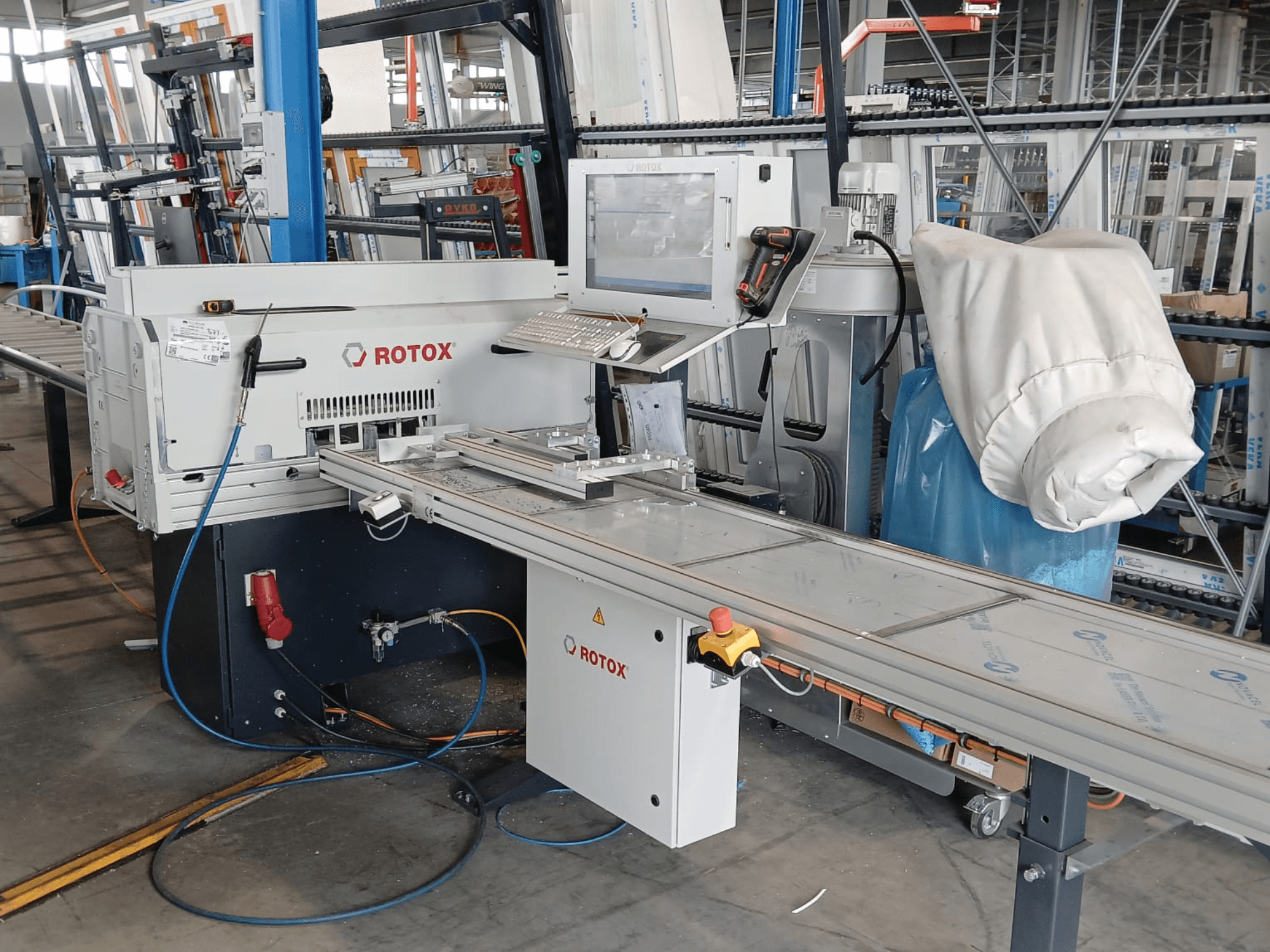 Vista frontale di una macchina per la lavorazione della plastica Rotox GLA401 con pannello di controllo, nastro trasportatore e tubi flessibili in vista, in un ambiente industriale.