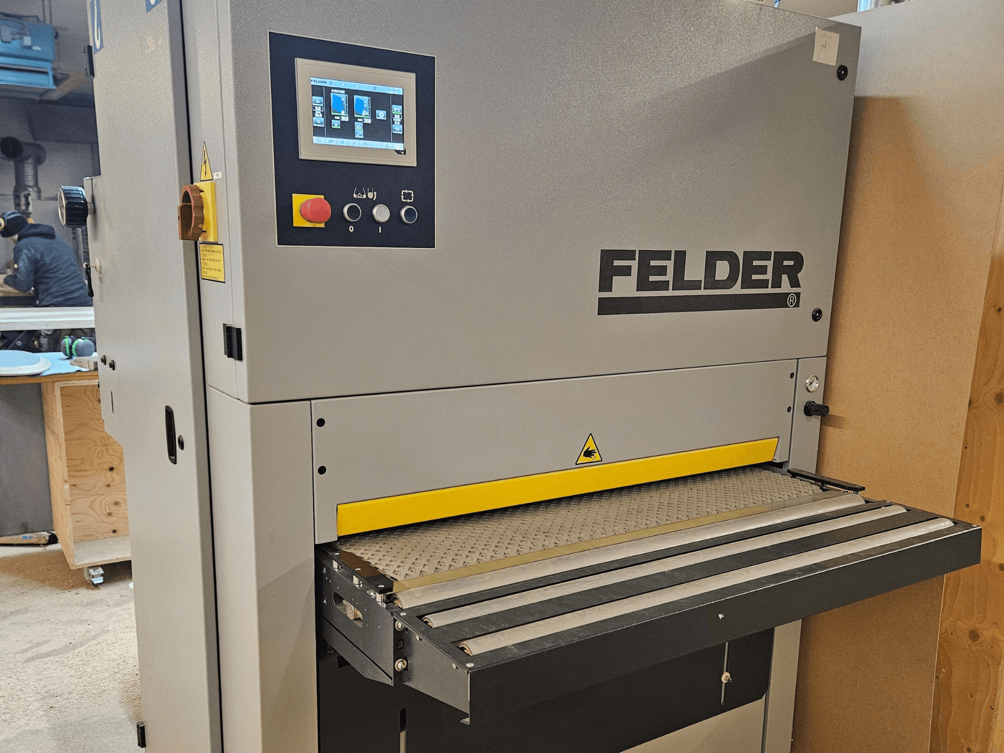 Macchina per la lavorazione del legno FELDER in vista frontale, con pannello di controllo digitale e tavola di alimentazione gialla con avvisi di sicurezza.