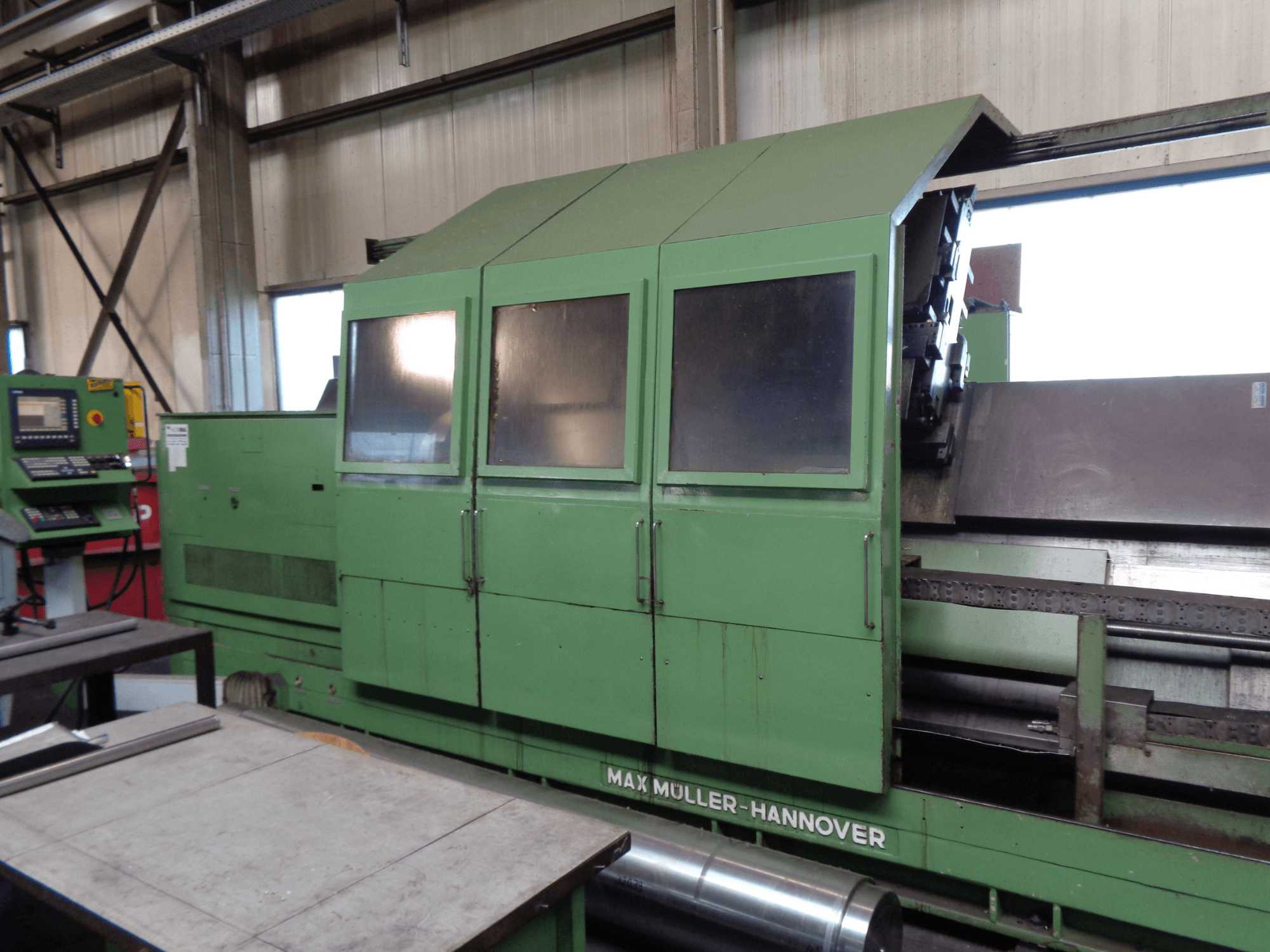 Centro di tornitura-fresatura MAX MULLER 3000 di colore verde, vista laterale con pannello di controllo. Sono visibili l'ampia area di lavorazione e la cabina con finestrini.