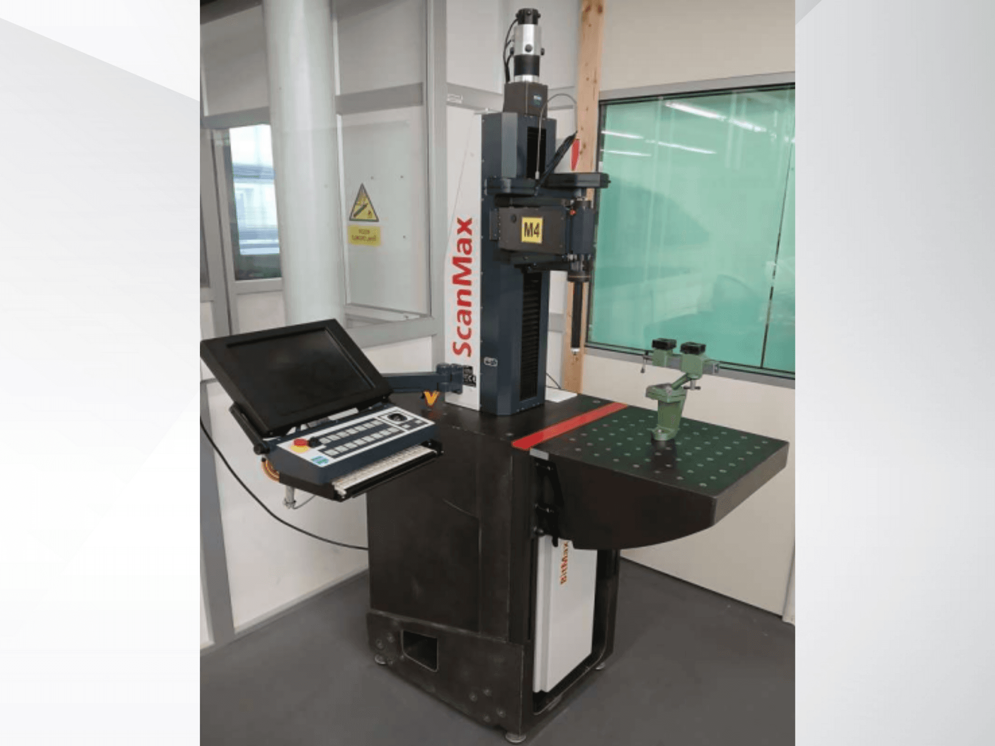 Macchina di misura ScanMax M4, vista frontale con pannello di controllo e dispositivo di calibrazione verde su un tavolo di lavoro tratteggiato.