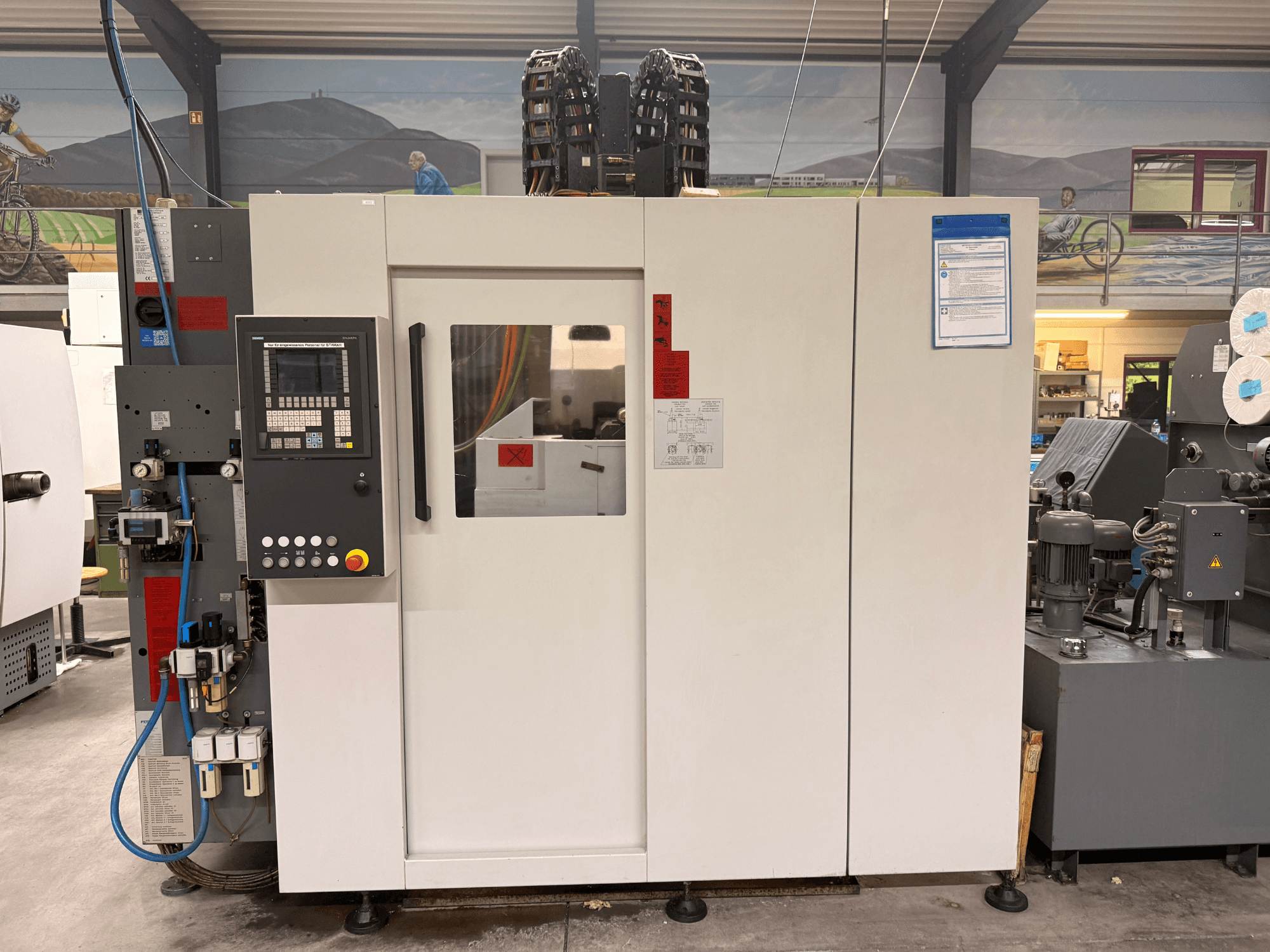 Centro di lavoro CNC bianco con pannello di controllo, vista frontale, con pulsanti e display digitale, in un'officina.