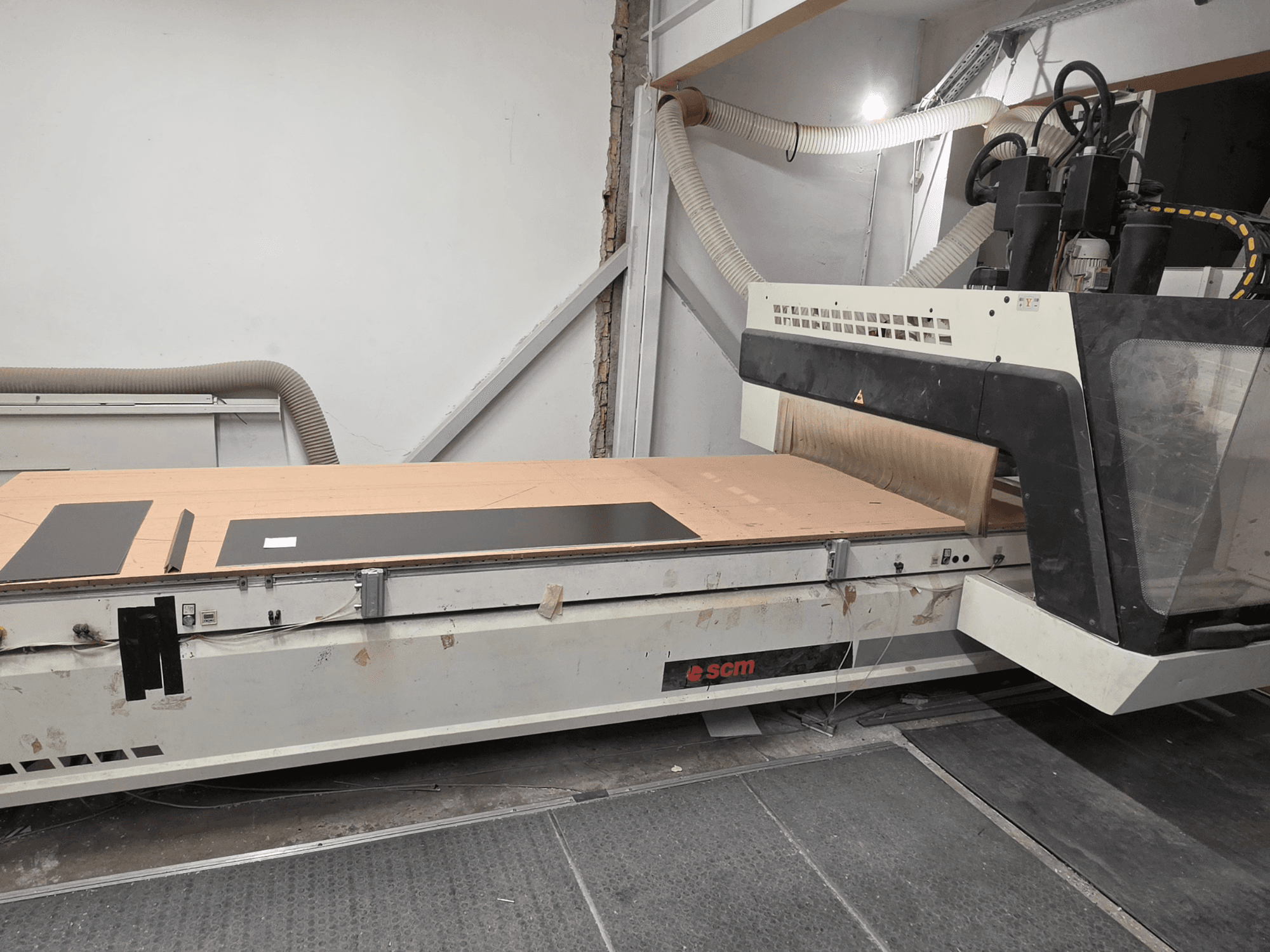 SCM RECORD 132: centro di lavorazione del legno a controllo numerico visto di profilo, dotato di un piano di lavoro piatto con pezzi in lavorazione di colore nero e sistema di aspirazione delle polveri.