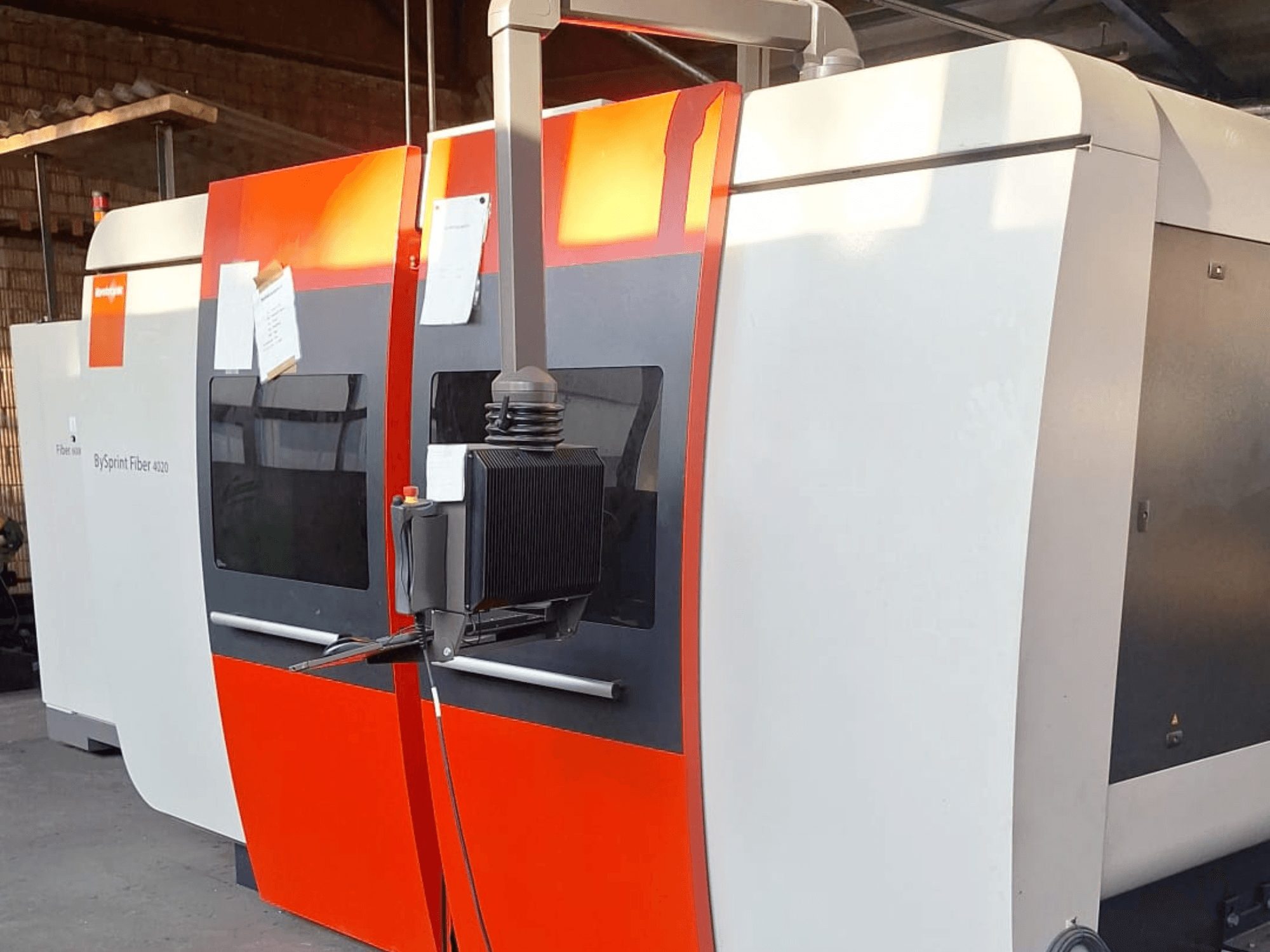 Macchina da taglio laser BySprint Fiber 4020, vista laterale, con esterno rosso e bianco, pannello di controllo dettagliato visibile.