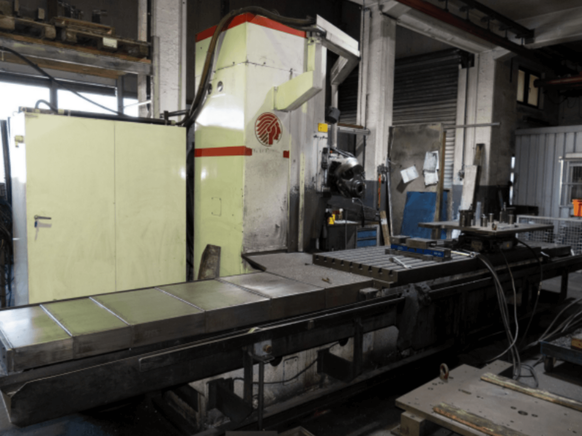 Fresatrice industriale con un grande tavolo, vista laterale, che mostra i comandi e gli accessori in un'officina.