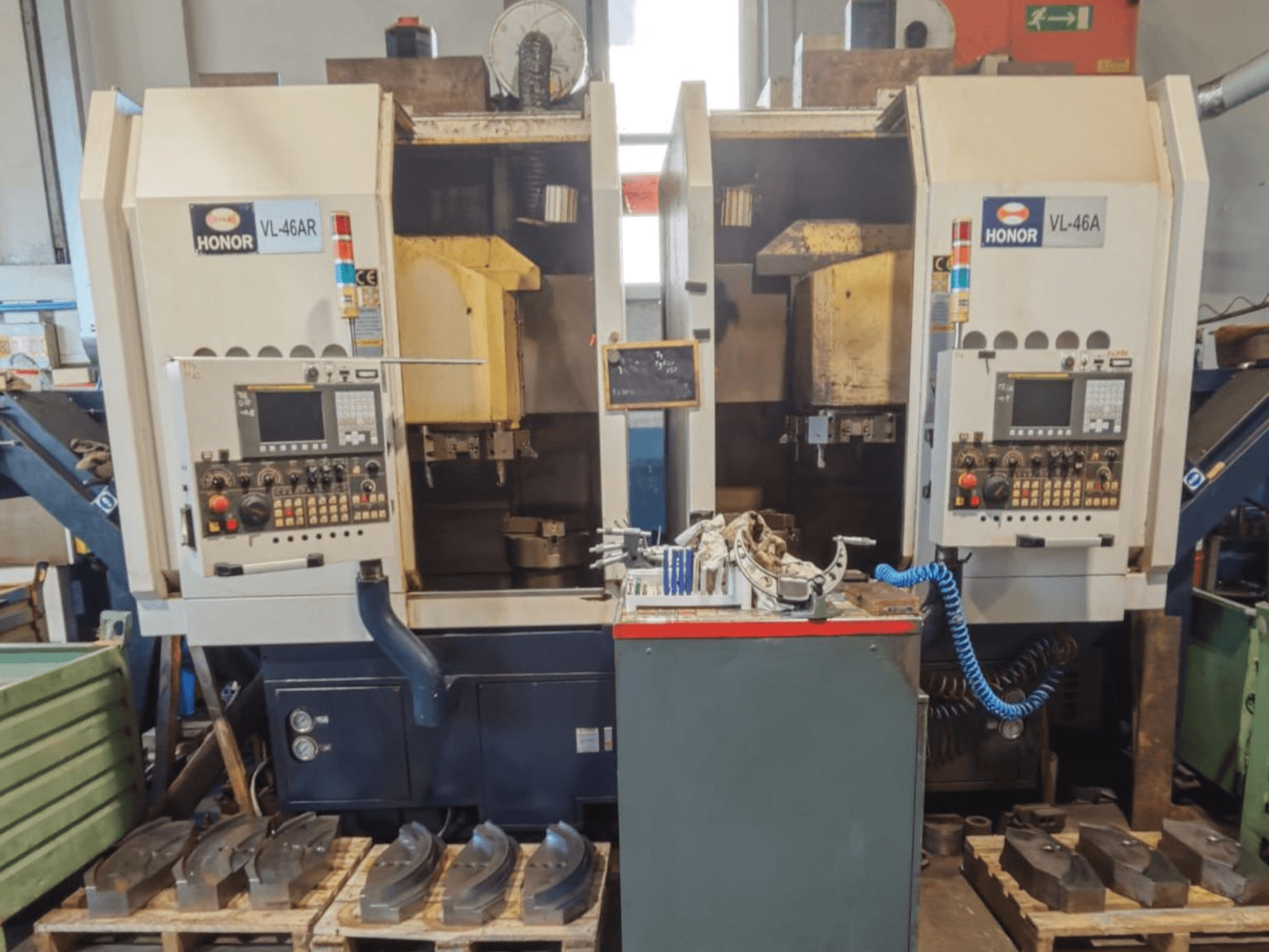 Vista frontale del tornio verticale HONOR SEIKI VL 46A, con il pannello di controllo e i componenti circostanti disposti su pallet di legno.