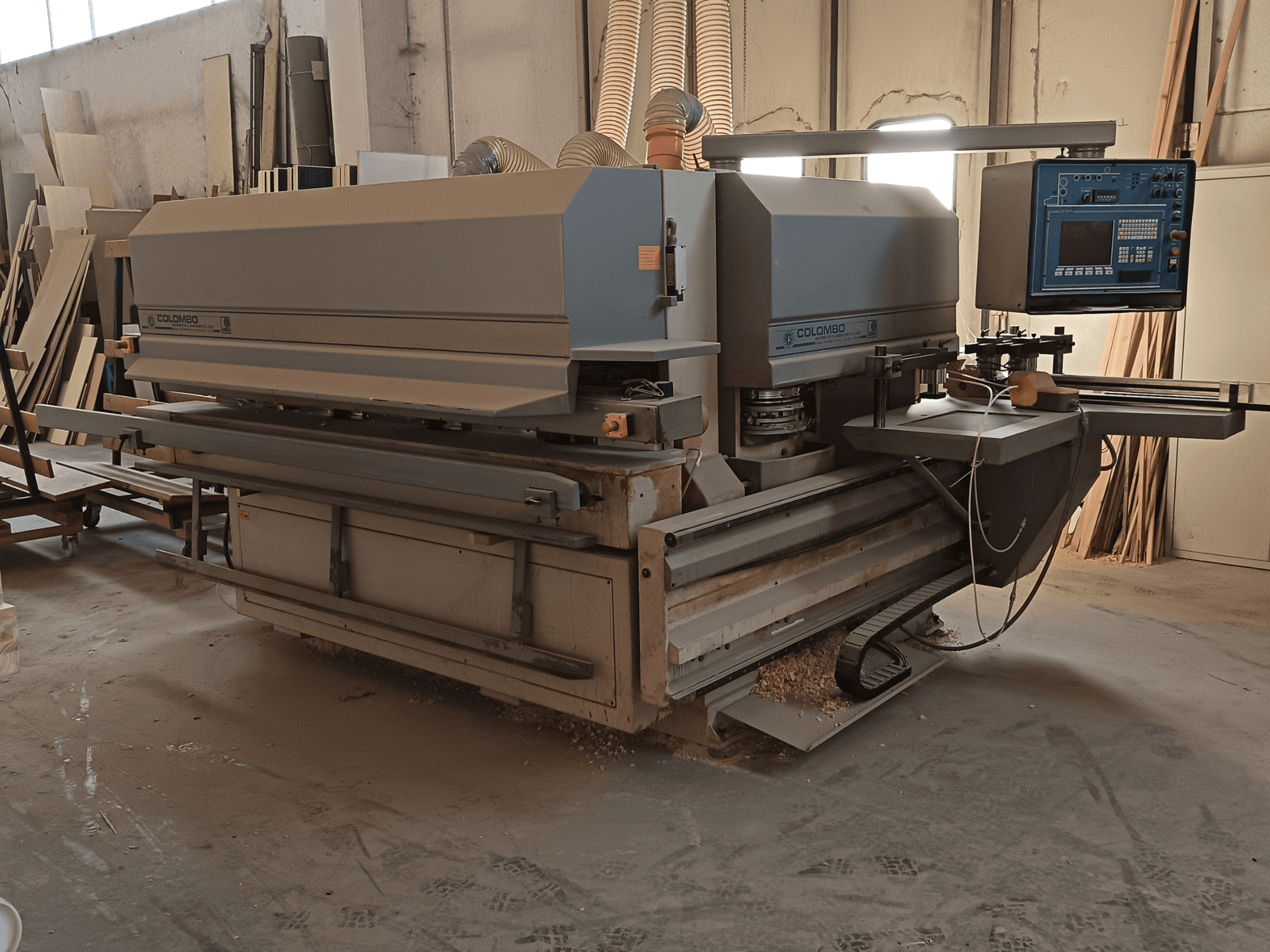 Macchina Colombo per la lavorazione del legno, vista laterale, che mostra il pannello di controllo, le lame di taglio e l'accumulo di polvere in officina.