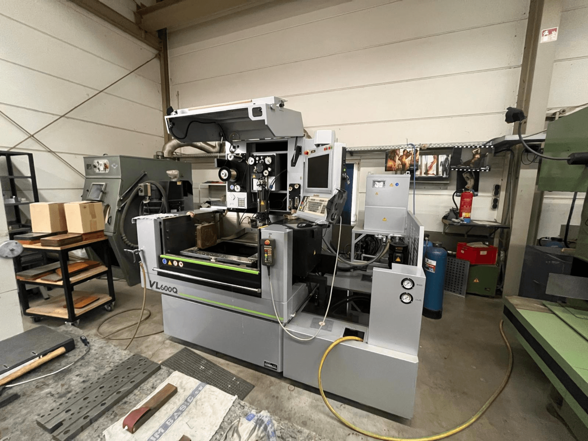 Macchina CNC VL600Q in un'officina, vista frontale, con pannello di controllo, materiale in posizione e vari utensili nelle vicinanze.