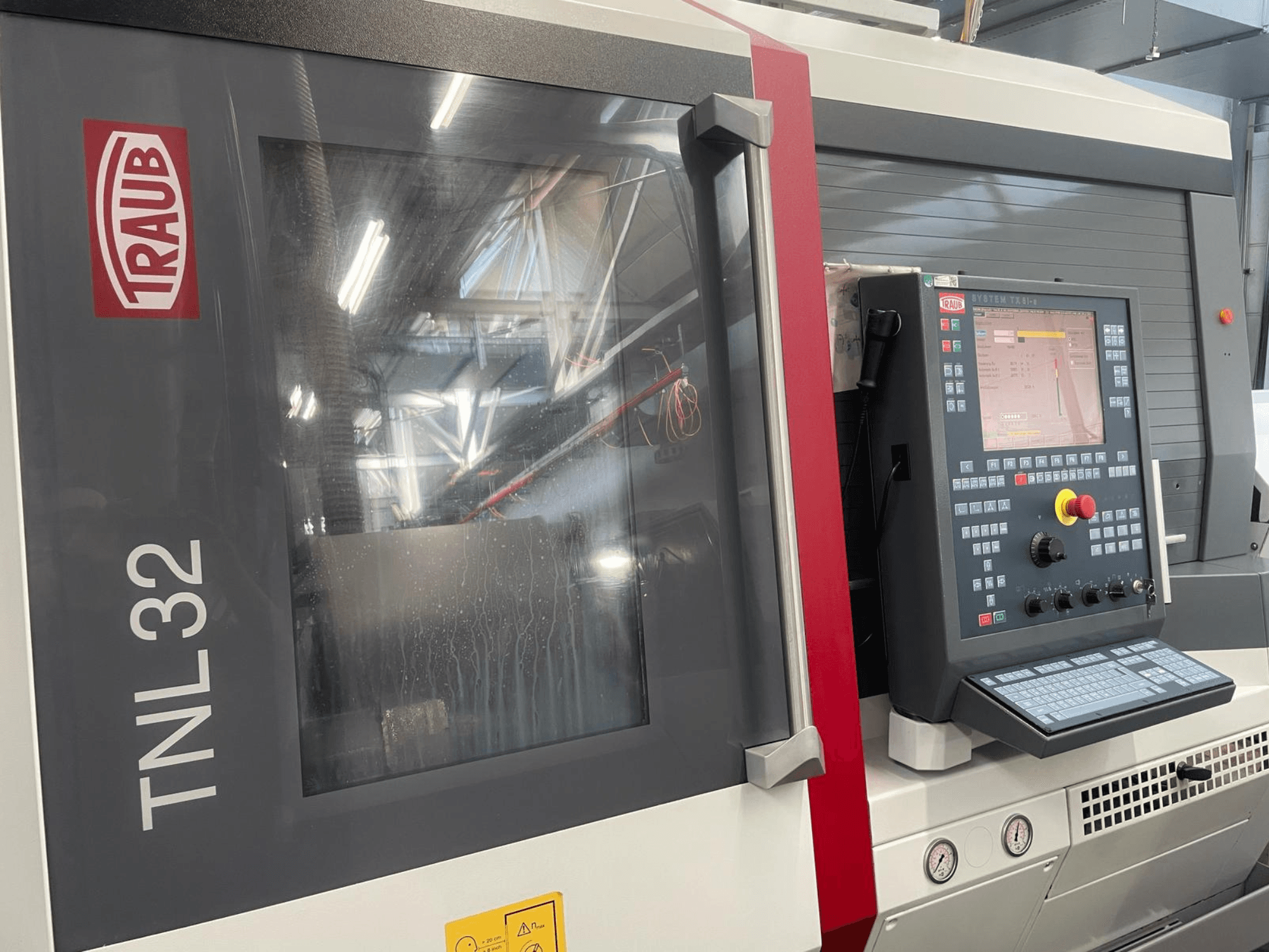 Vista frontale del tornio CNC Traub TNL32, con pannello di controllo con pulsanti, schermo e un elegante involucro metallico.