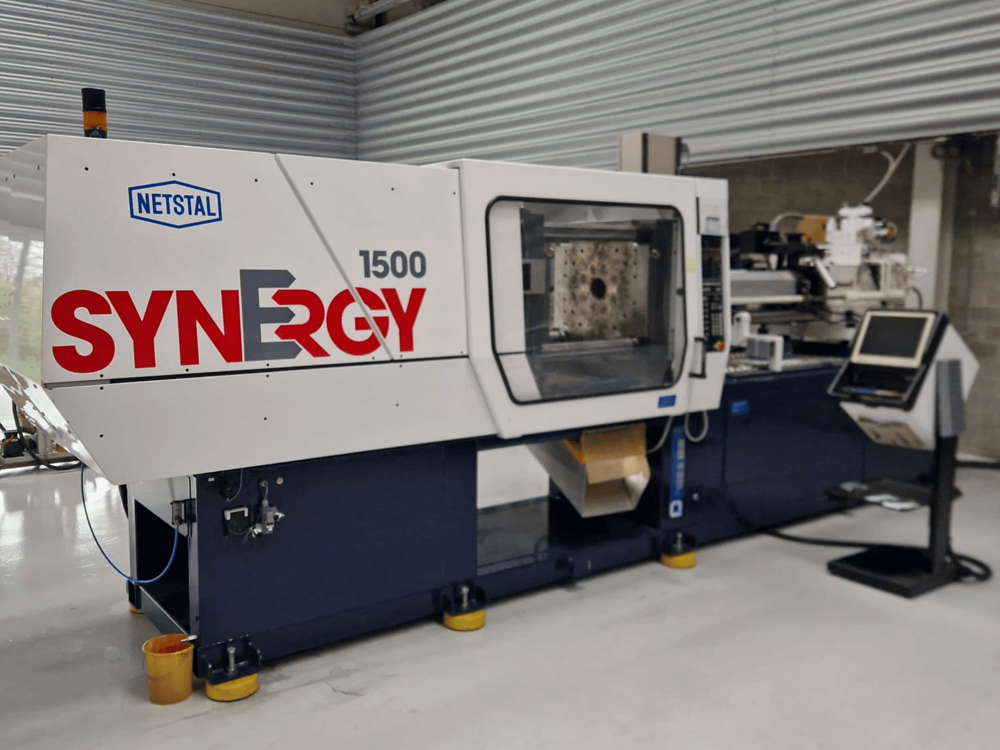 Macchina ad iniezione idraulica Netstal Synergy 1500-460, vista frontale, con pannello di controllo e area di iniezione aperta.