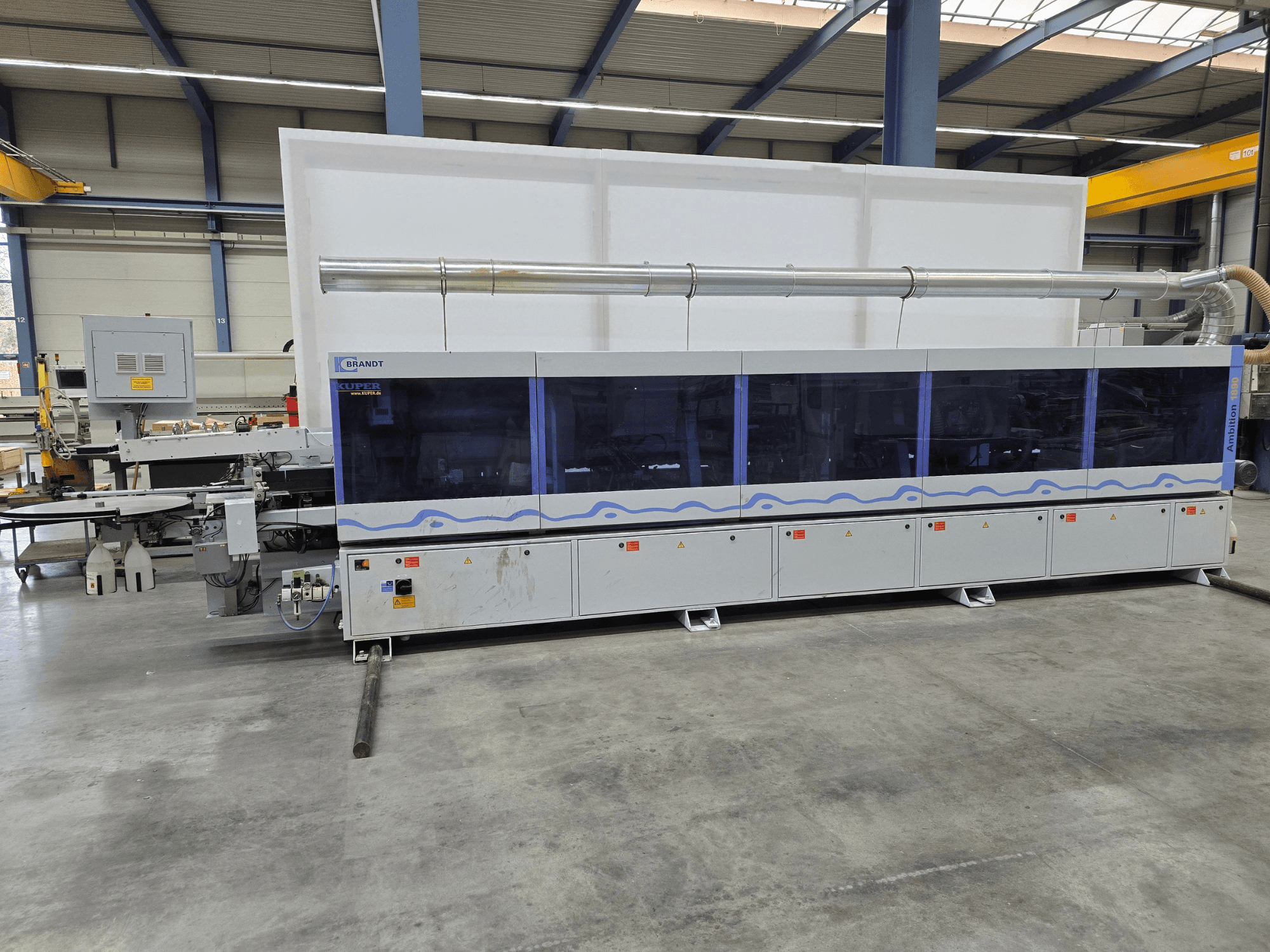Macchina Brandt KUPER in uno stabilimento, vista frontale con pannelli trasparenti, con pulsanti di controllo e avvisi di sicurezza.