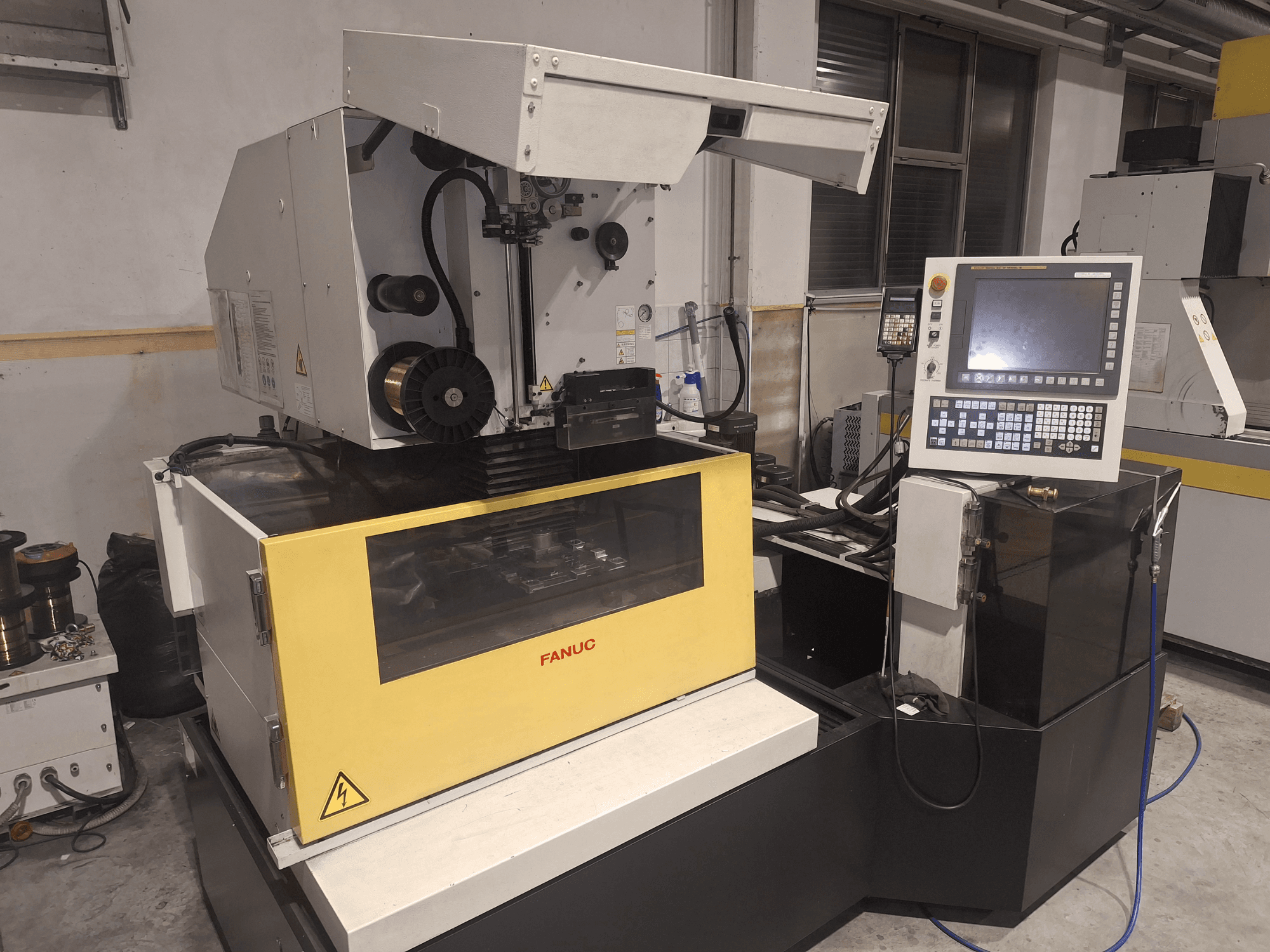 Macchina CNC FANUC in vista frontale con coperchio aperto, che rivela l'area di lavoro e il pannello di controllo sulla destra.