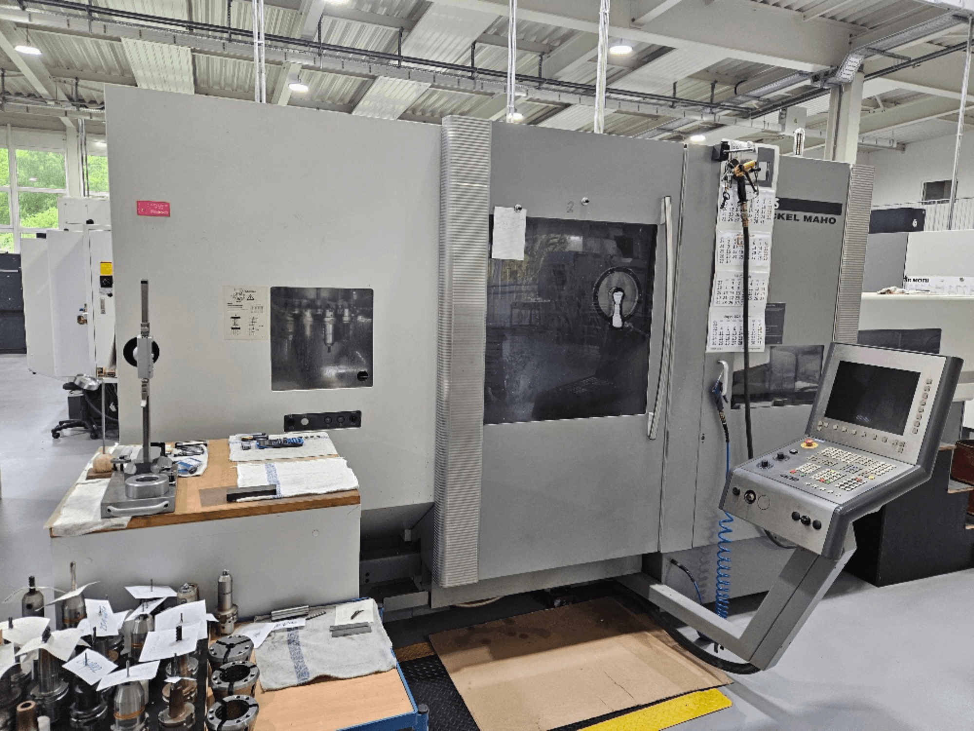 Vista frontale di una macchina DMG Mori DMU 70 con pannello di controllo, utensili su un tavolo di legno e vari pezzi nelle vicinanze.