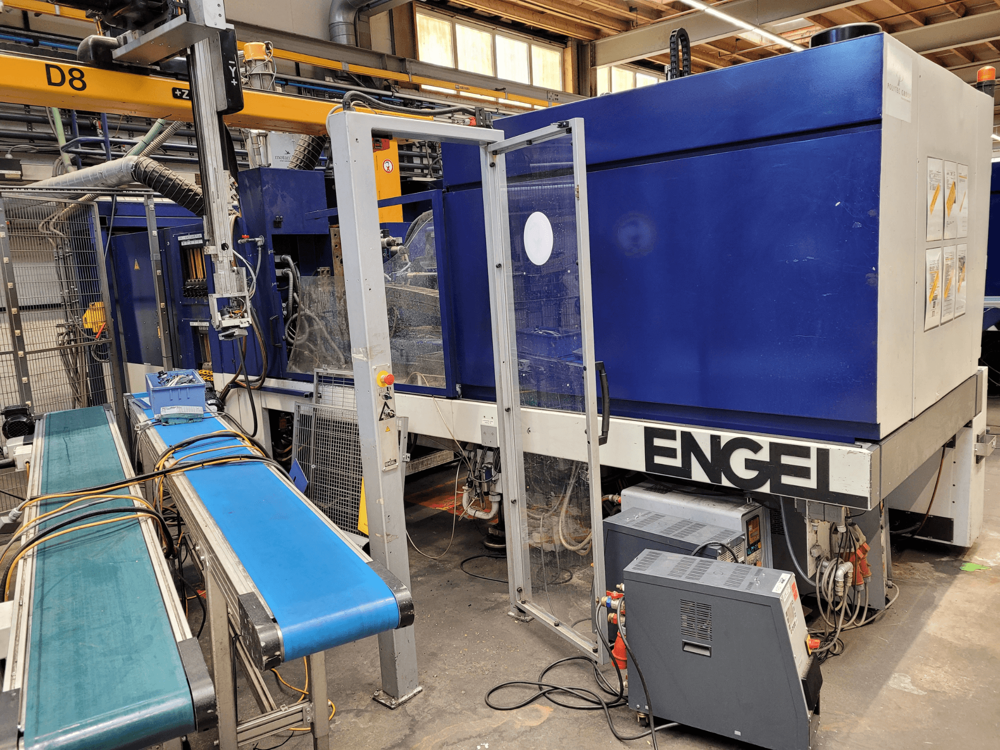 Macchina ENGEL blu con porta di sicurezza trasparente, vista laterale, dotata di pannello di controllo, nastro trasportatore e collegamenti elettrici visibili.