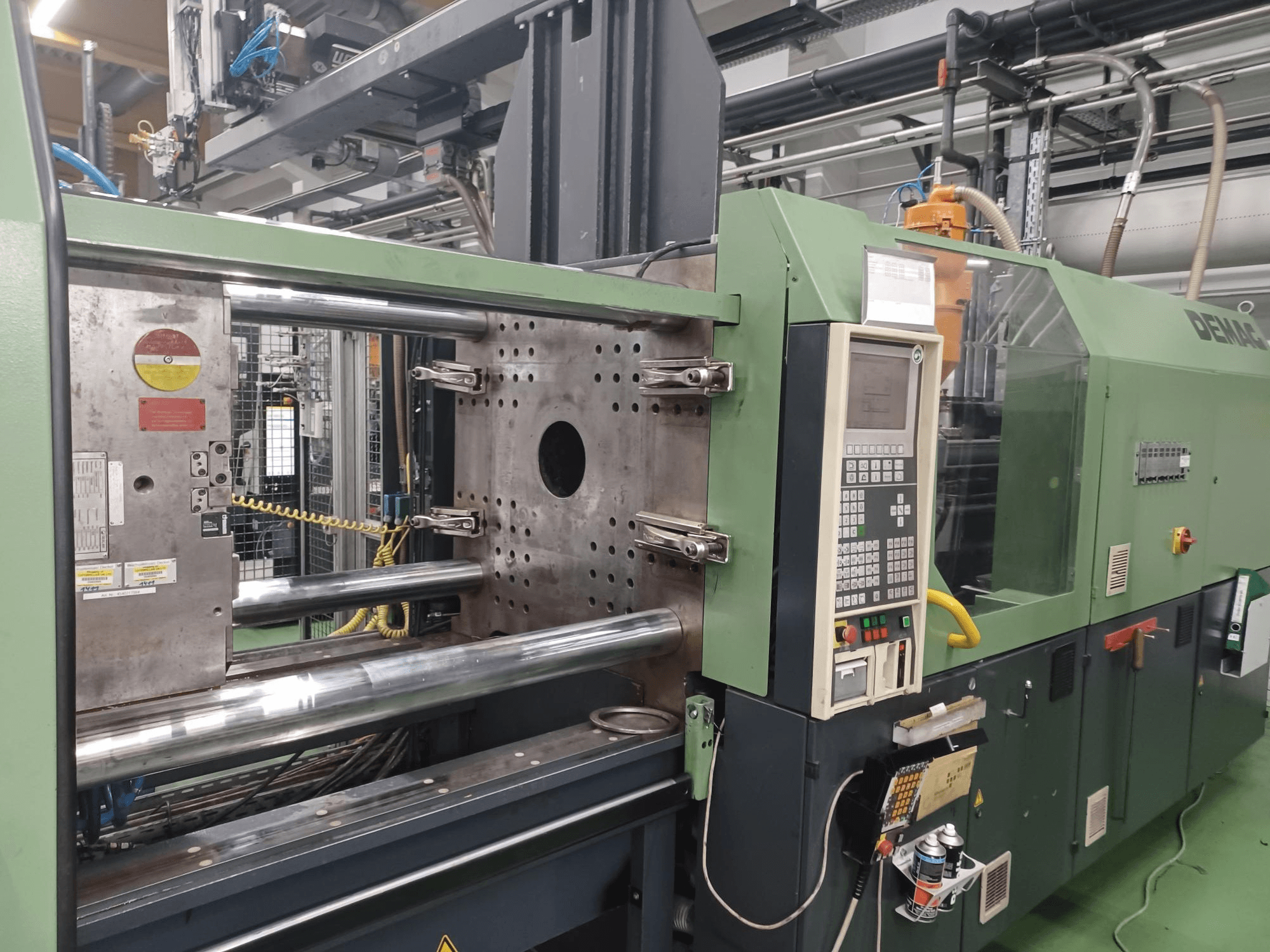 Macchina ad iniezione Demag, vista frontale, con pannello di controllo, cilindri idraulici metallici e caratteristiche di sicurezza.