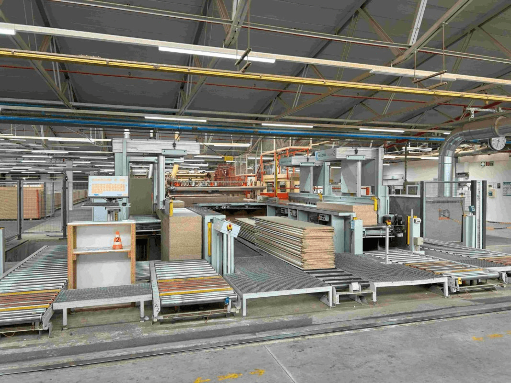 Interno di un impianto di produzione che mostra linee di assemblaggio con pannelli e macchinari impilati, vista frontale, illuminazione intensa, attrezzature moderne.