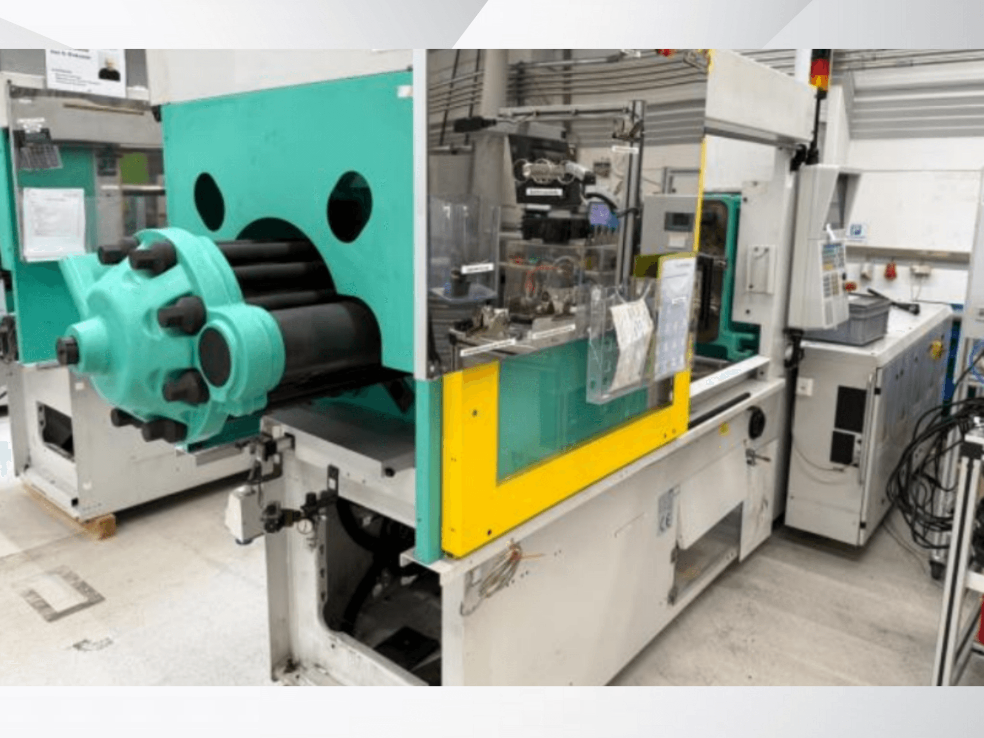 Macchina per lo stampaggio a iniezione, blu chiaro e giallo, vista frontale, con stampo a vista e pannello di controllo con etichette.