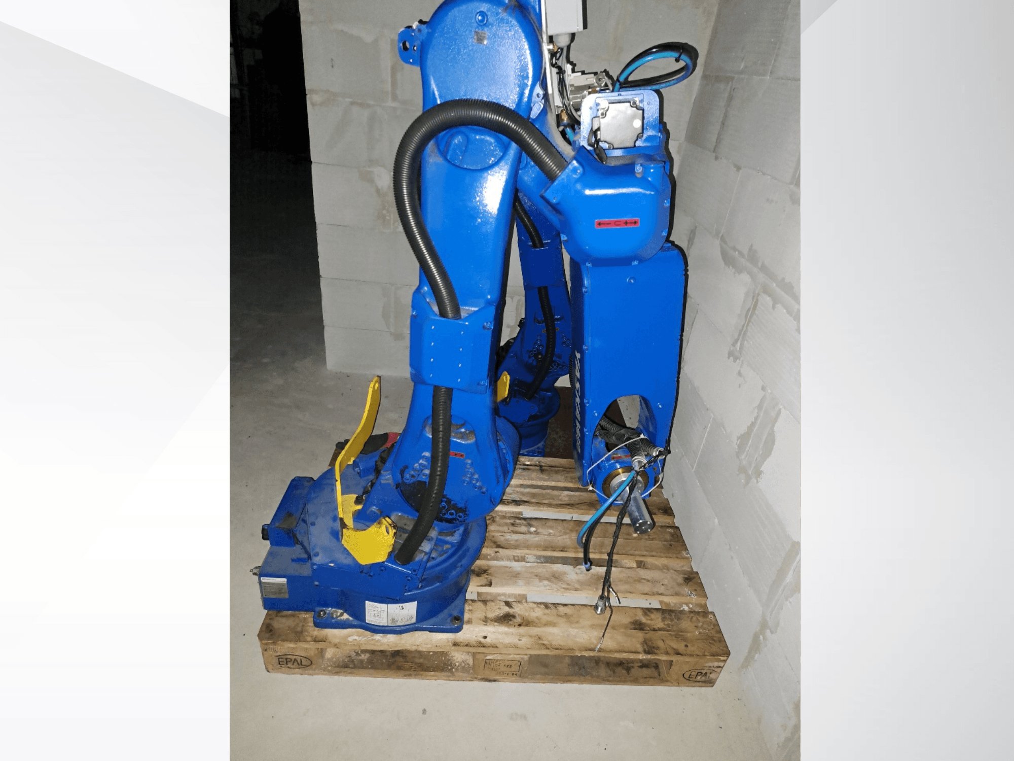 Braccio robotico Yaskawa Motoman GP25 di colore blu, visto di profilo su un pallet di legno, con cavi e giunti meccanici.