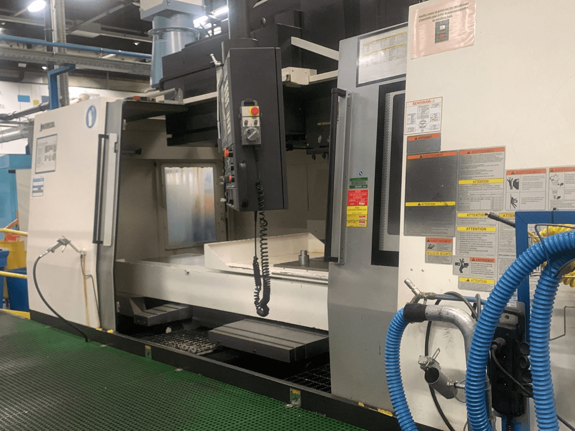 Centro di lavorazione verticale Okuma Millac 852 VII, vista frontale, con pannello di controllo, zona mandrino ed etichette di sicurezza.