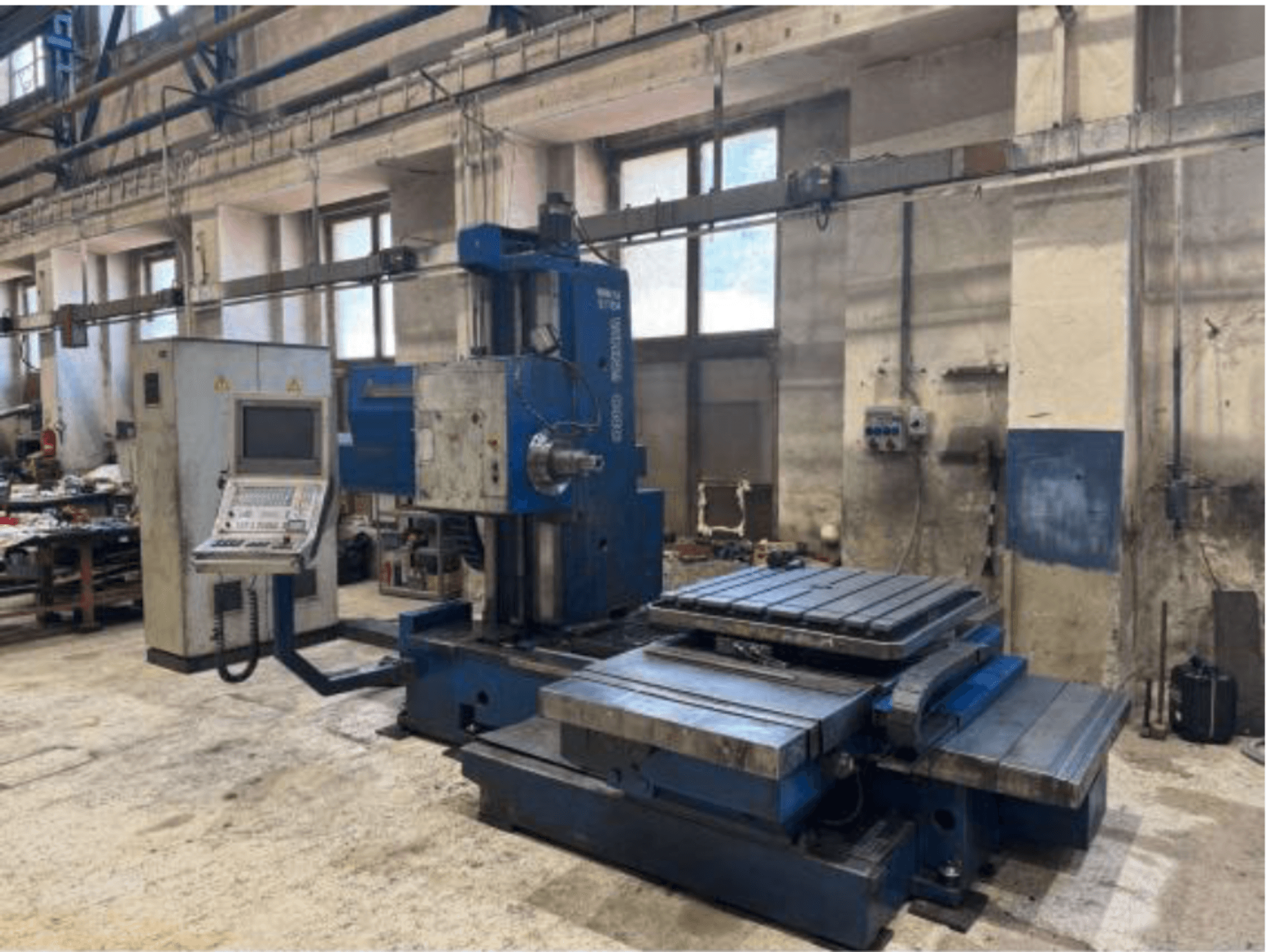 Vista frontale della alesatrice CNC TOS WHN 9 B, dotata di pannello di controllo e ampio piano di lavoro, collocata in un ambiente di officina.