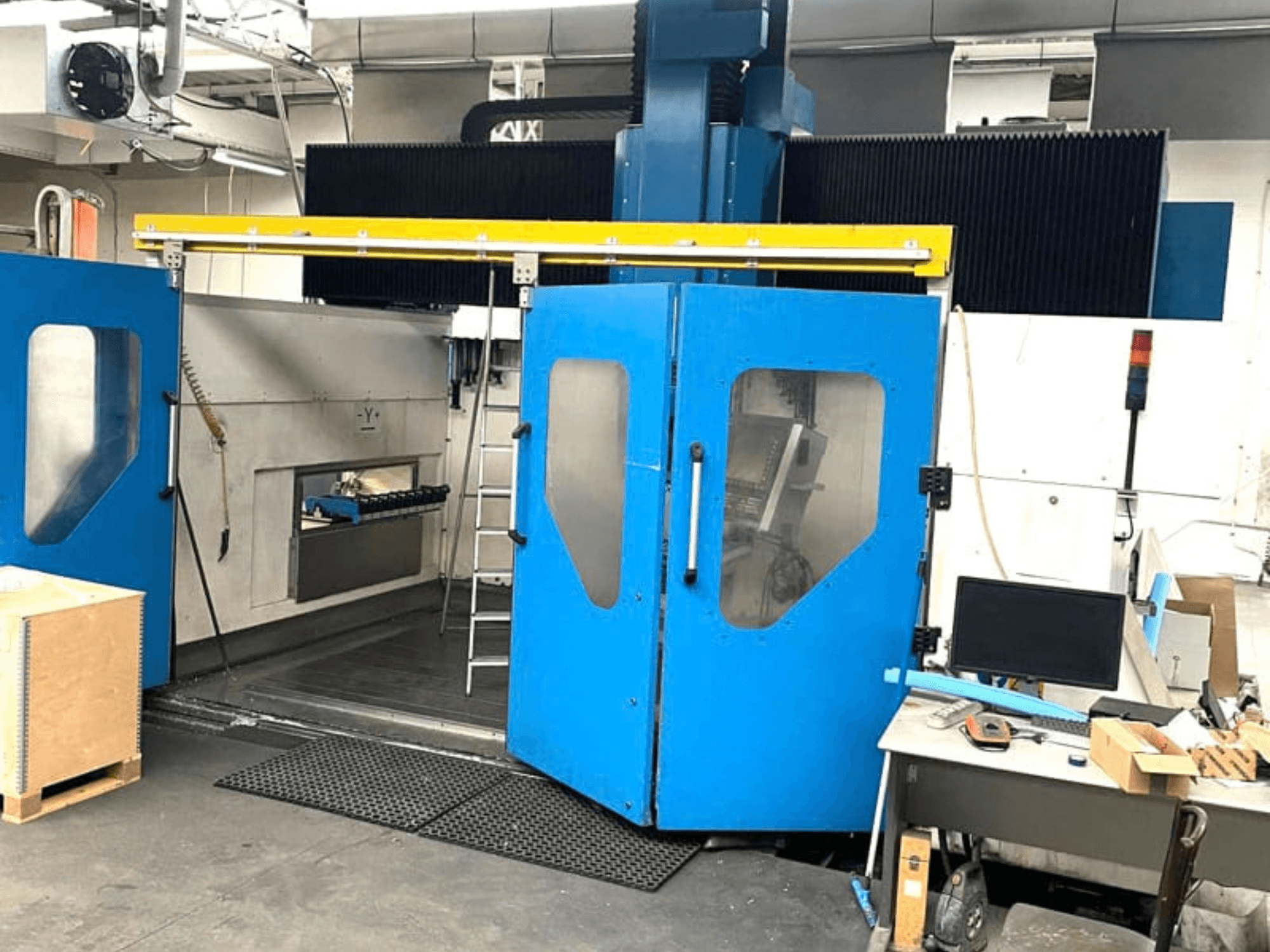 Vista frontale del centro di lavorazione verticale TECHMILL LABOR SHAPE 3220 con le porte blu aperte, che lasciano intravedere l'area di lavoro all'interno.