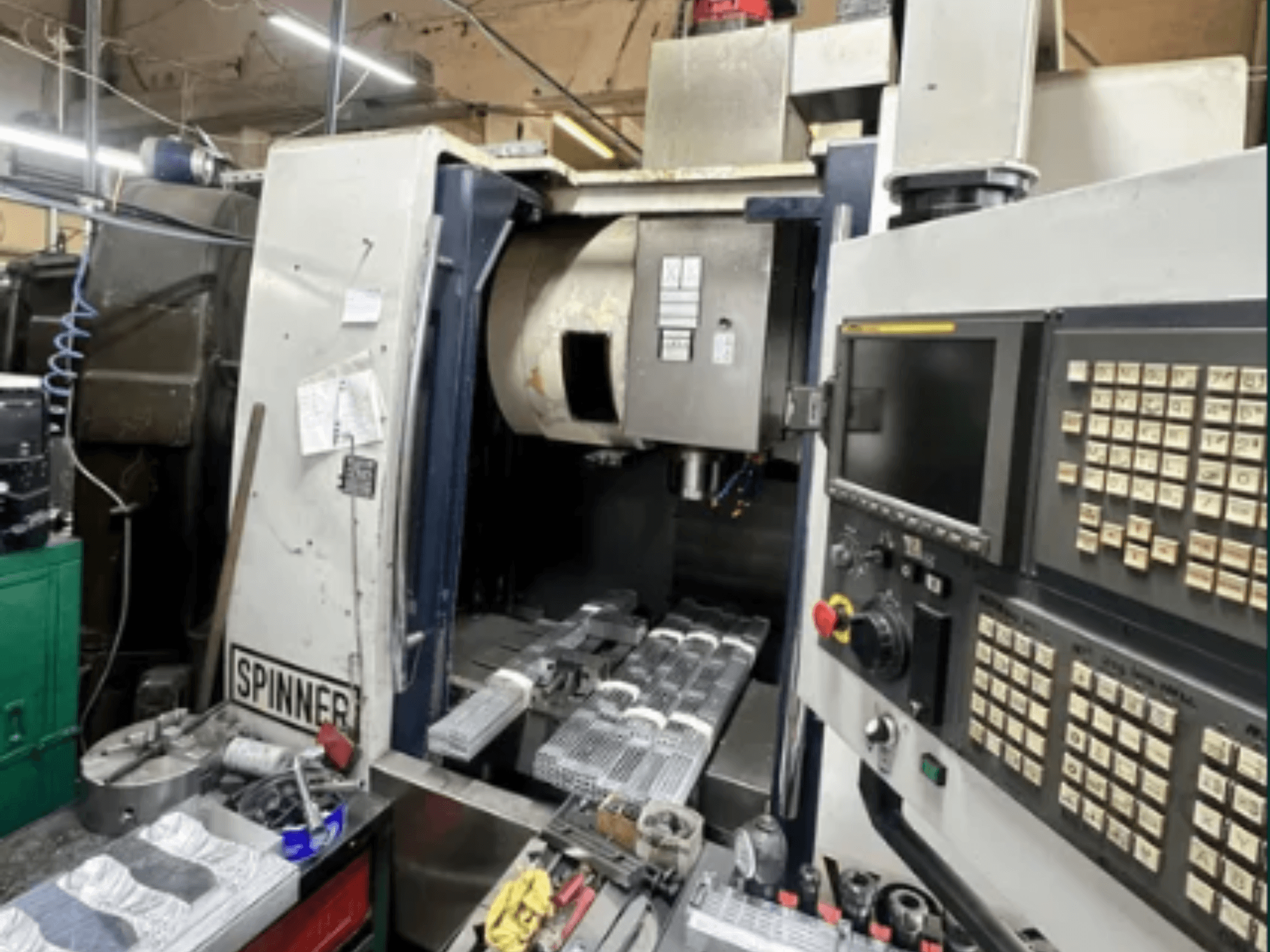 Macchina CNC di Spinner, vista frontale; dispone di interfaccia touchscreen, utensili sull'area di lavoro e pezzi lavorati pronti per la lavorazione.