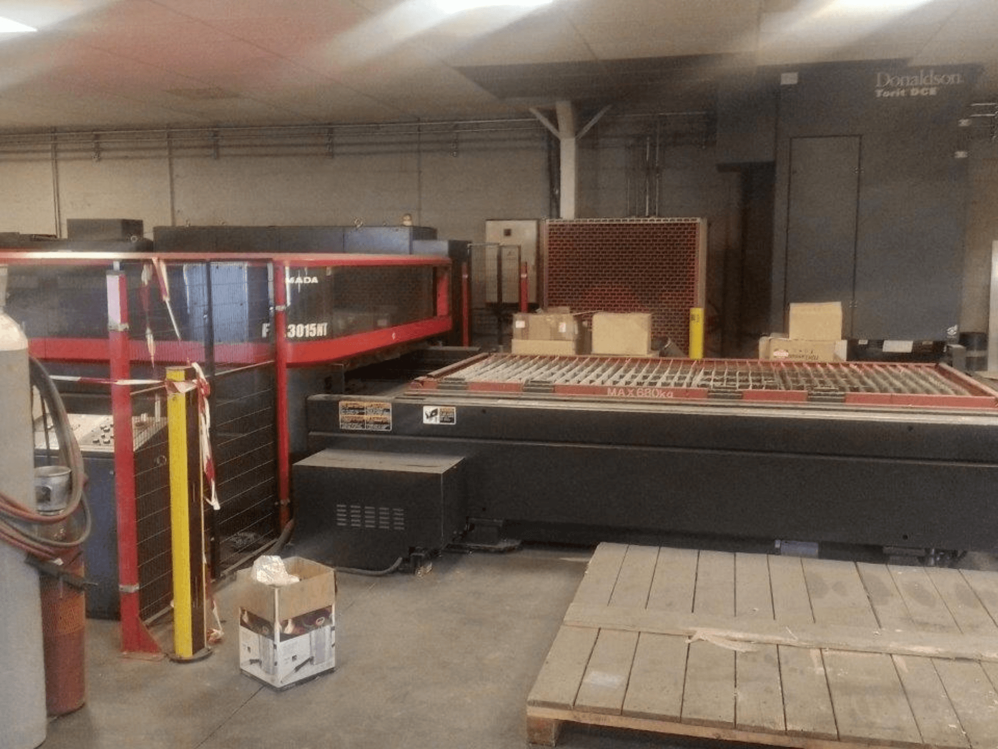 Macchina per il taglio laser a CO₂ AMADA FOL 3015 NT, vista frontale; cabina di sicurezza rossa, piano di lavoro con griglia, ambiente industriale.