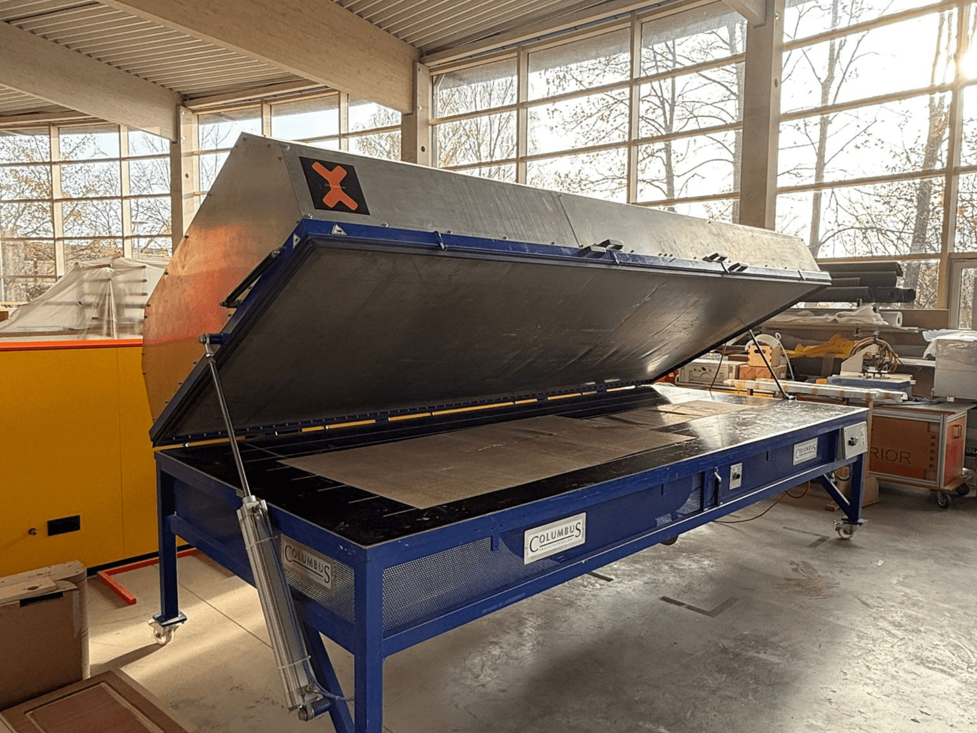 Pressa a vuoto Columbus in un'officina, vista frontale con il grande piano angolare aperto, che mostra una superficie piana e macchinari dettagliati.