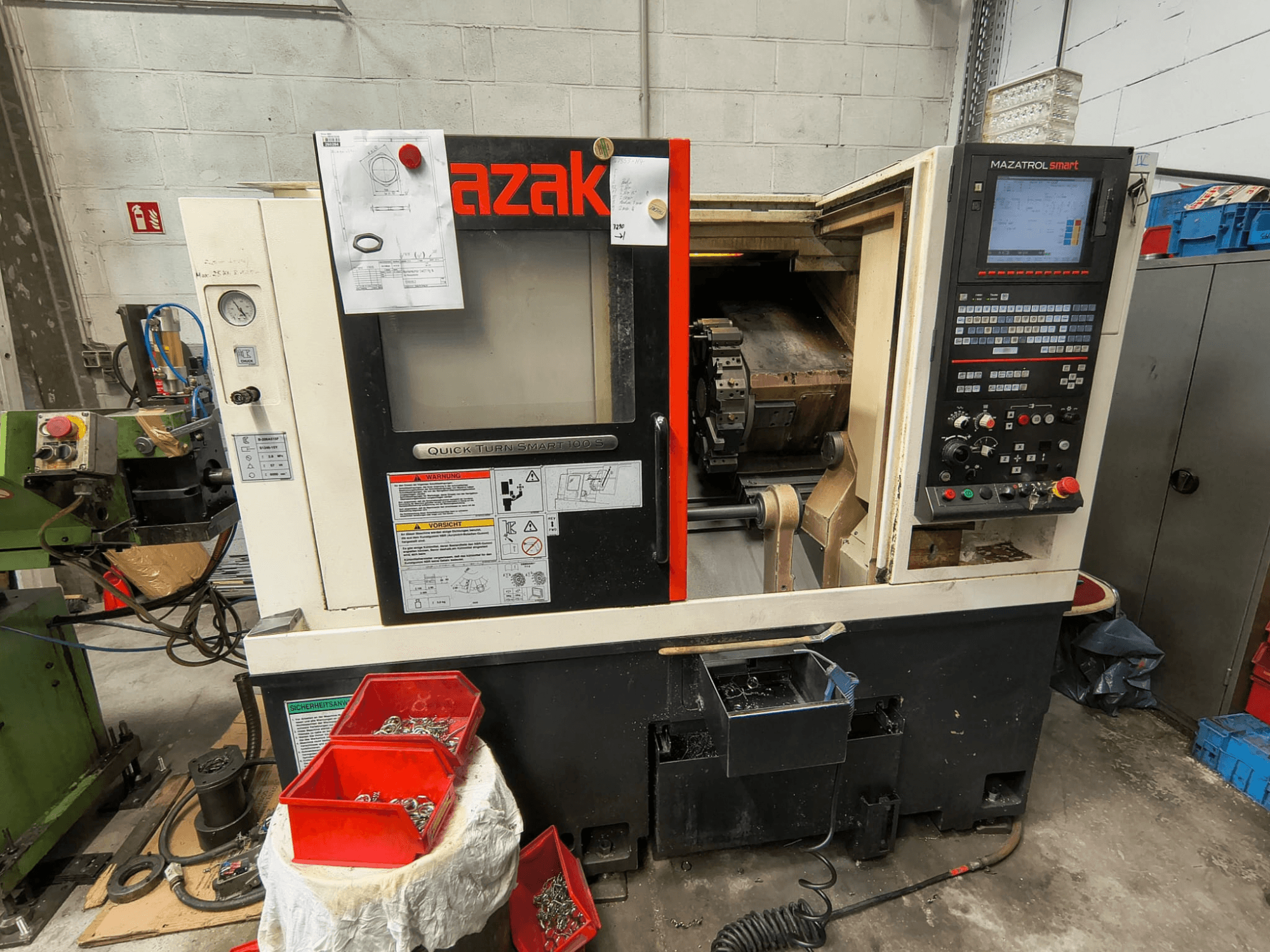 Mazak Quick Turn Smart 100 S, vista laterale che mostra il pannello di controllo, il vassoio per il liquido di raffreddamento e i contenitori con le viti.