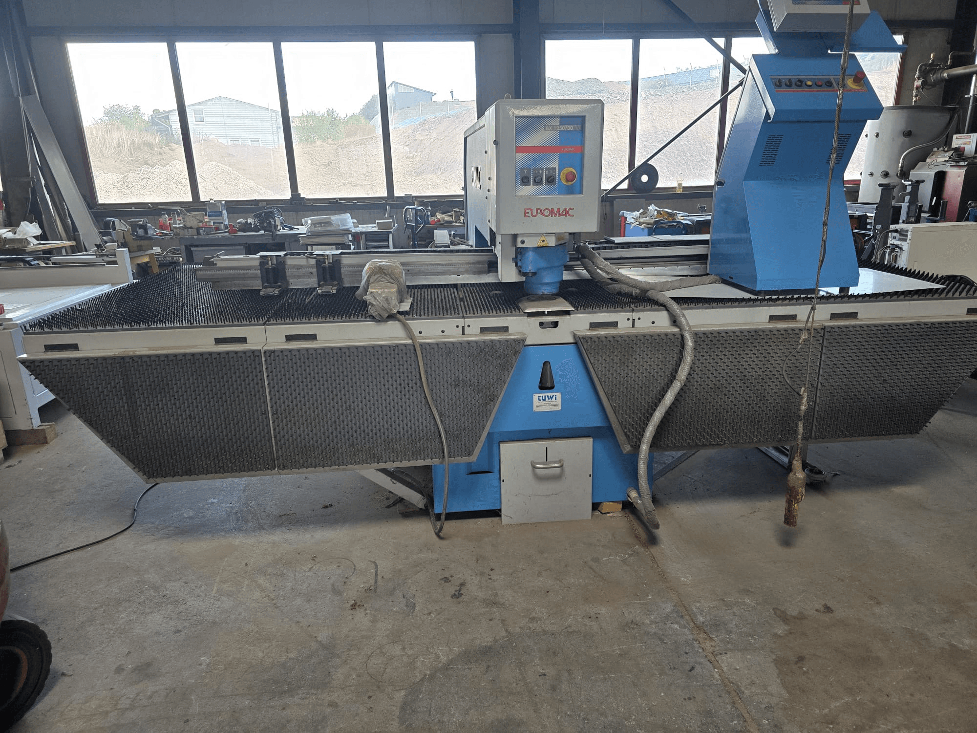 Punzonatrice CNC Euromac BX 1250/30 in un'officina, vista laterale che mostra i comandi della macchina, il design industriale e il piano di lavoro in metallo.