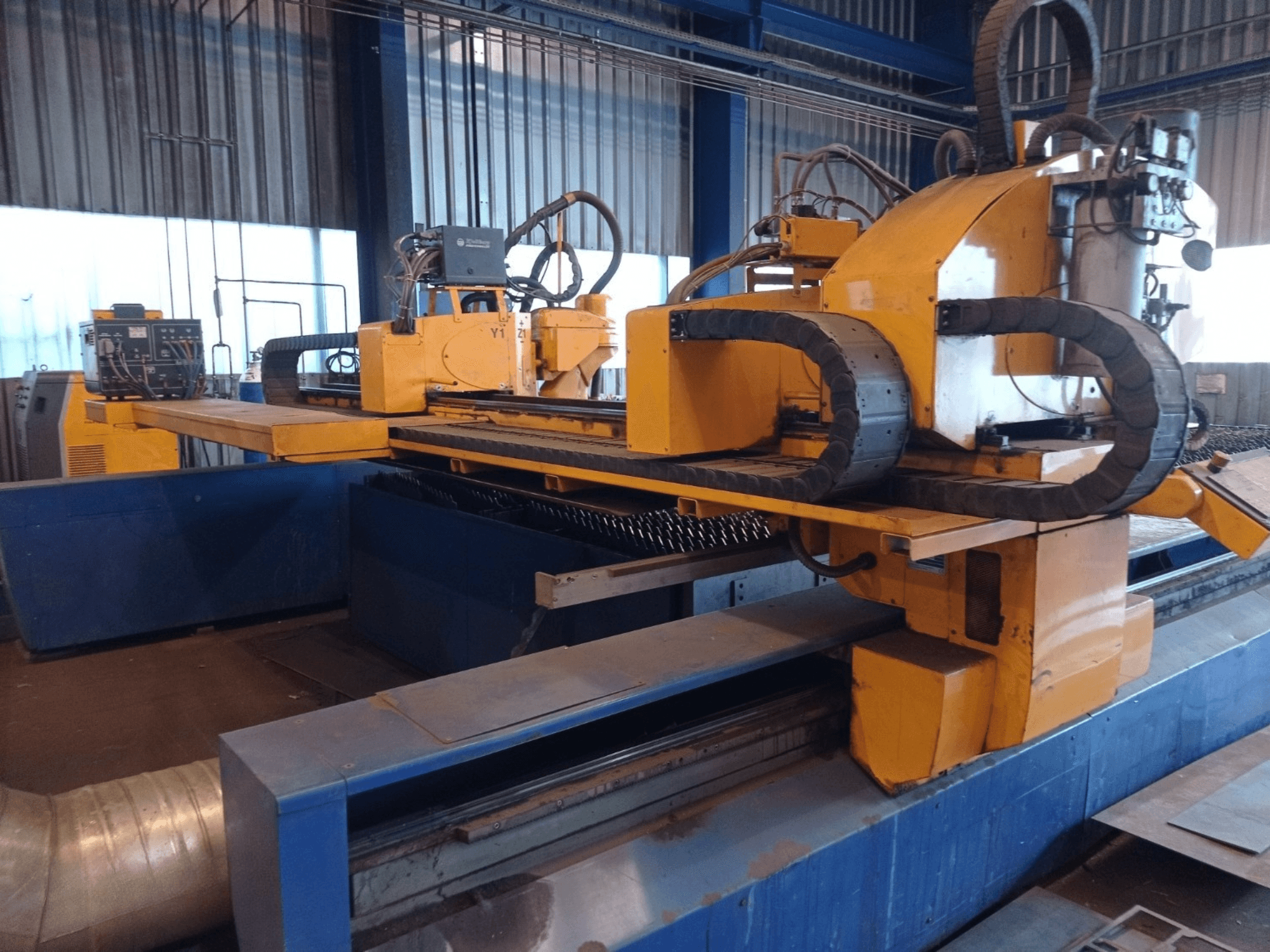 Macchina di taglio al plasma CNC gialla a due bracci orizzontali, vista dal davanti, con pannello di controllo e banco di taglio.