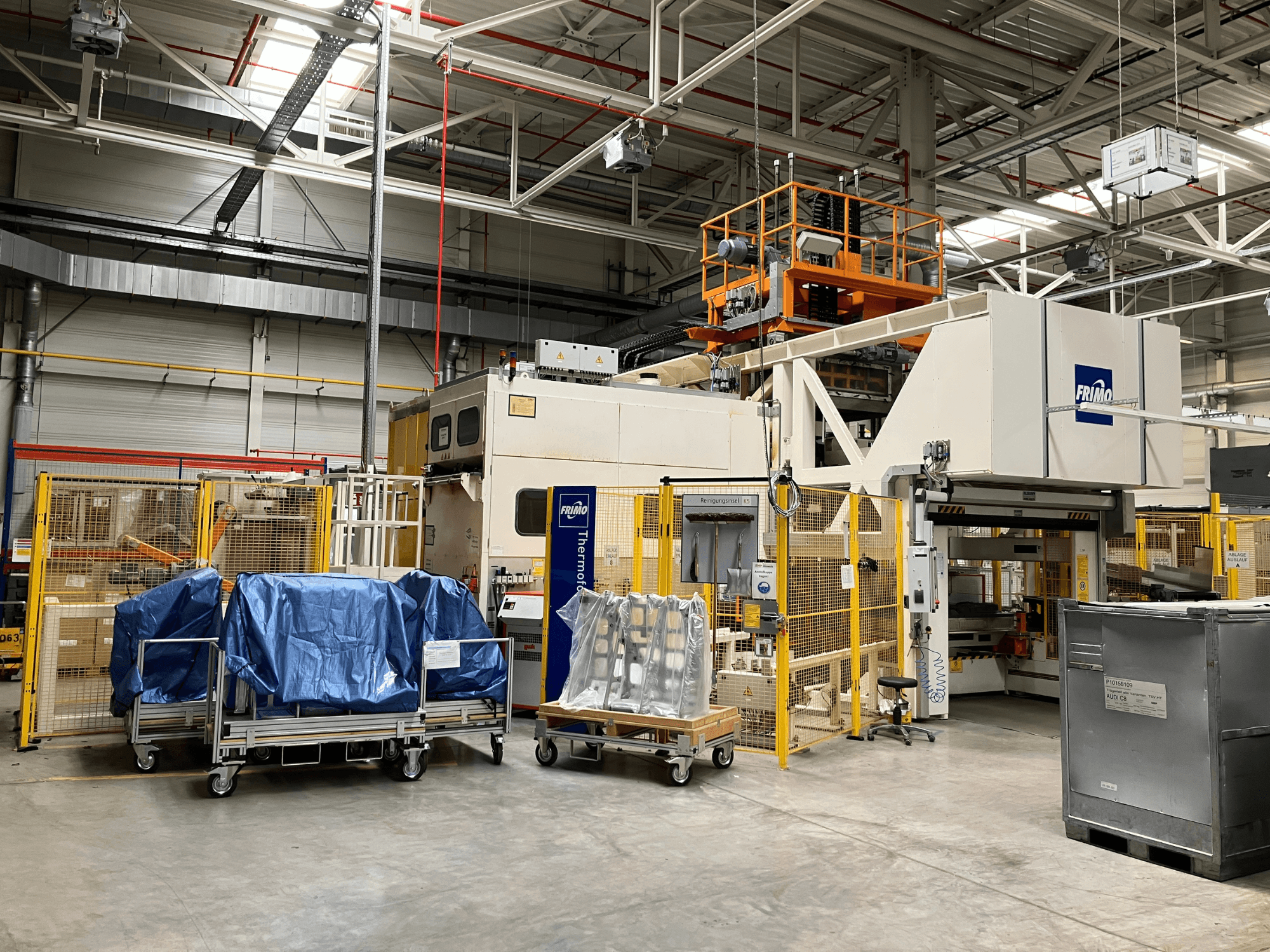 Macchina per la lavorazione della plastica FRIMO FTL 80/200 Fullflex in uno stabilimento, vista frontale con teloni blu e barriere di sicurezza visibili.